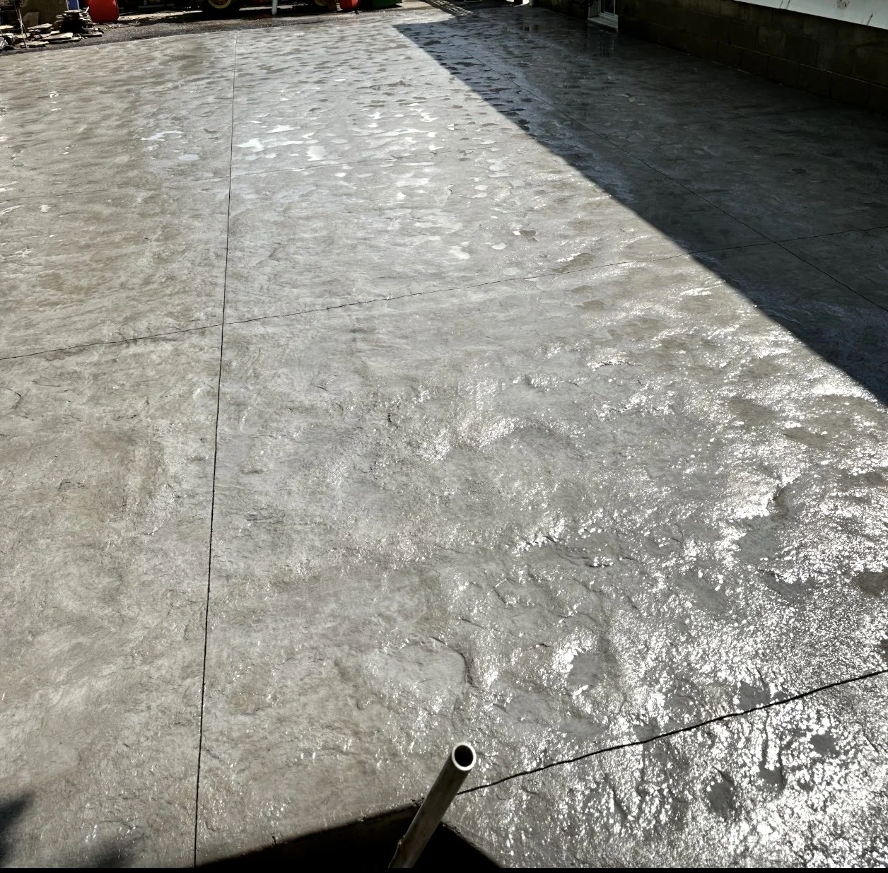 A stamped concrete surface, partially shadowed with sunlight reflecting off the wet surface.