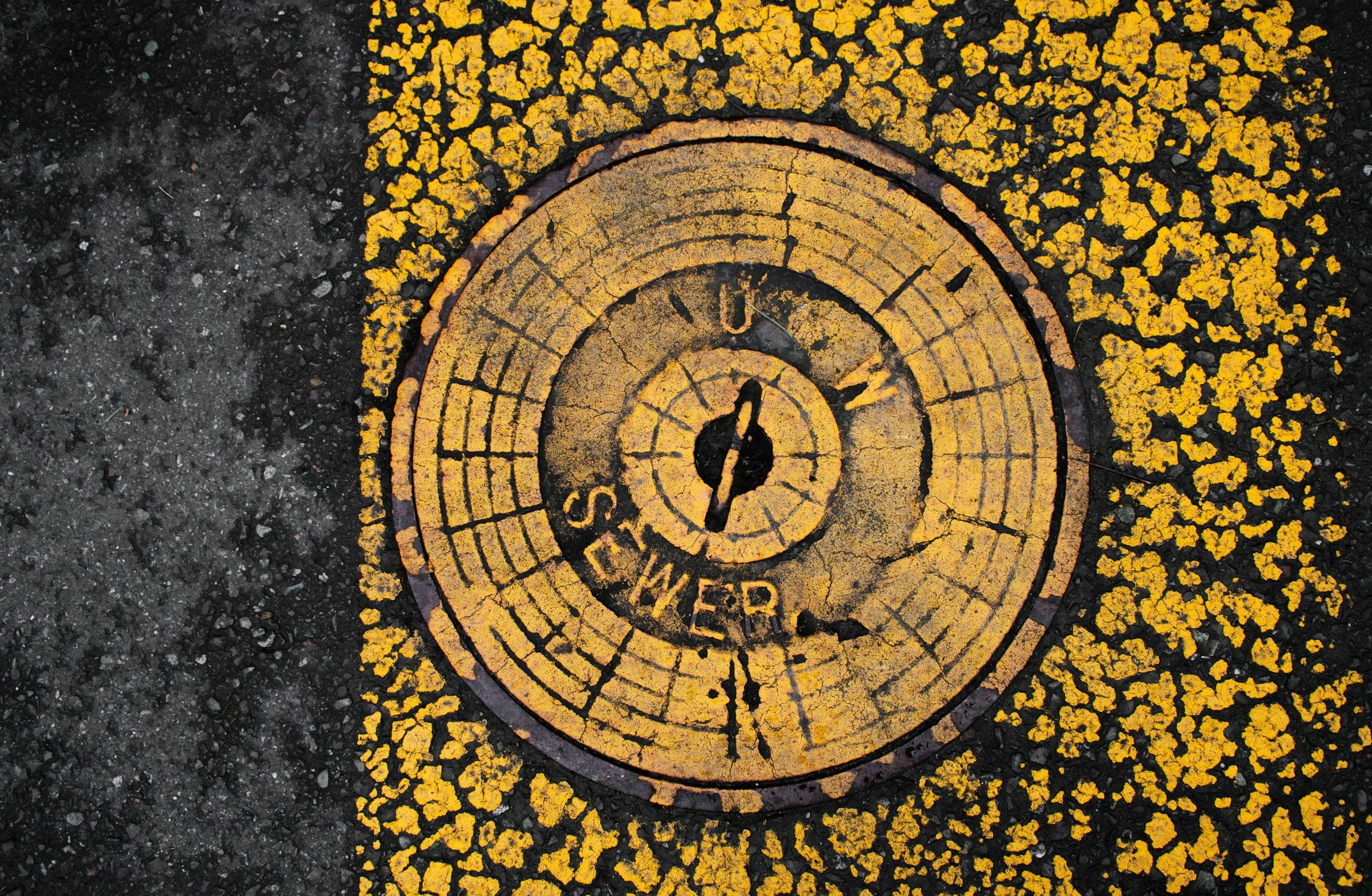 A yellow and black weatherproof circular map embedded in the asphalt of a street, showing directions with cardinal points and markings, with yellow paint around the edges.