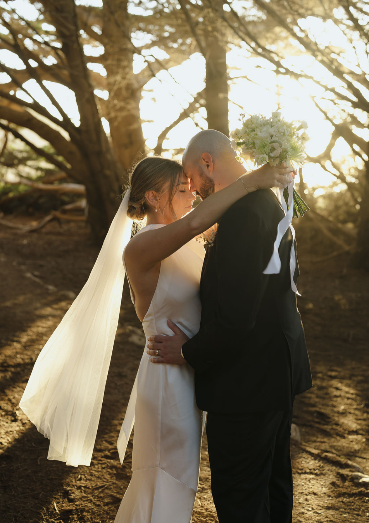 Bride with soft, glowing bridal makeup embracing her partner at sunset, looking calm, confident, and effortlessly beautiful on her wedding day