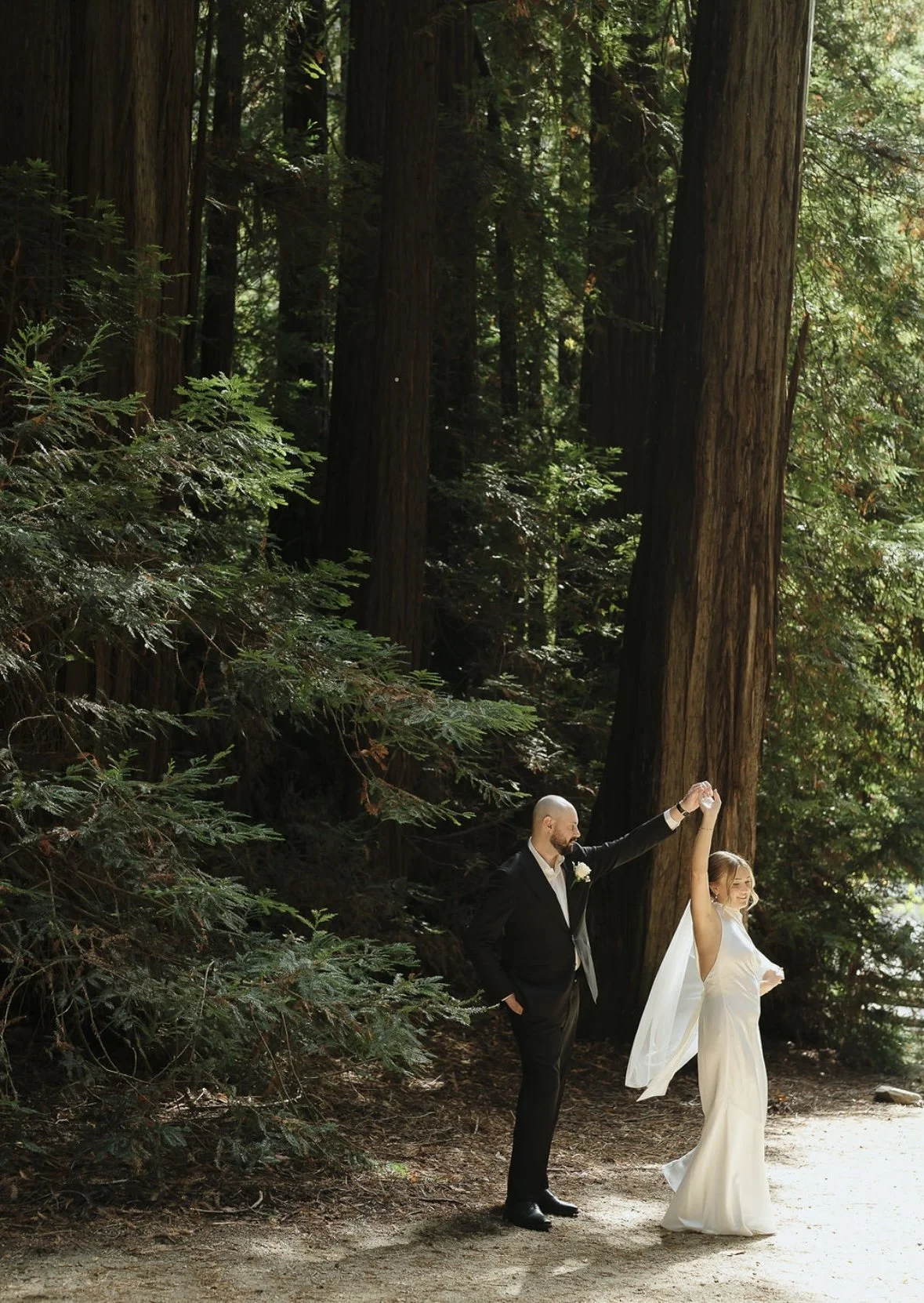 Bride with soft, radiant bridal makeup dancing with her partner in a romantic forest setting, looking confident, joyful, and effortlessly beautiful