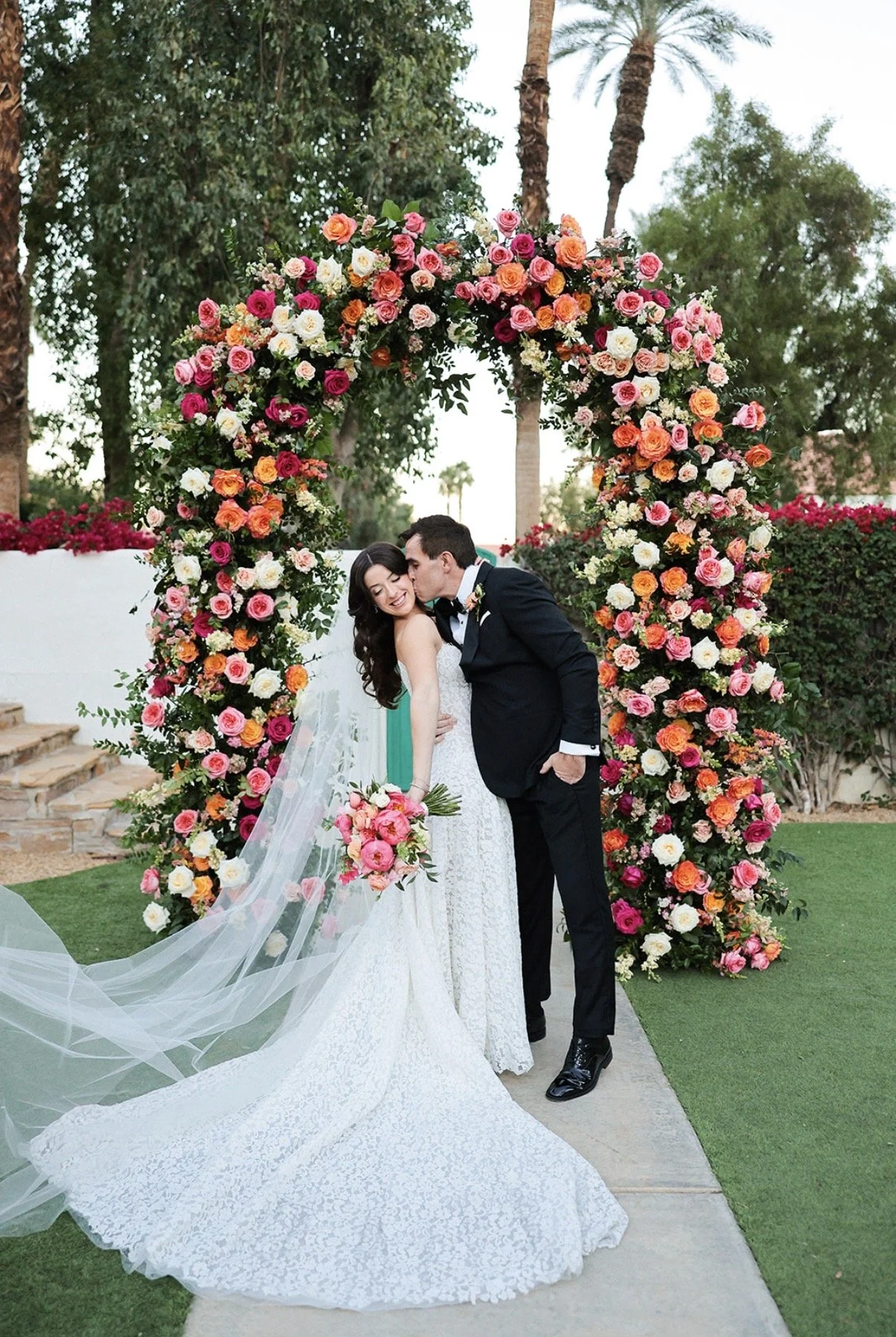 Bride with glowing, long-lasting wedding makeup sharing a romantic moment under a floral arch, looking confident and camera-ready