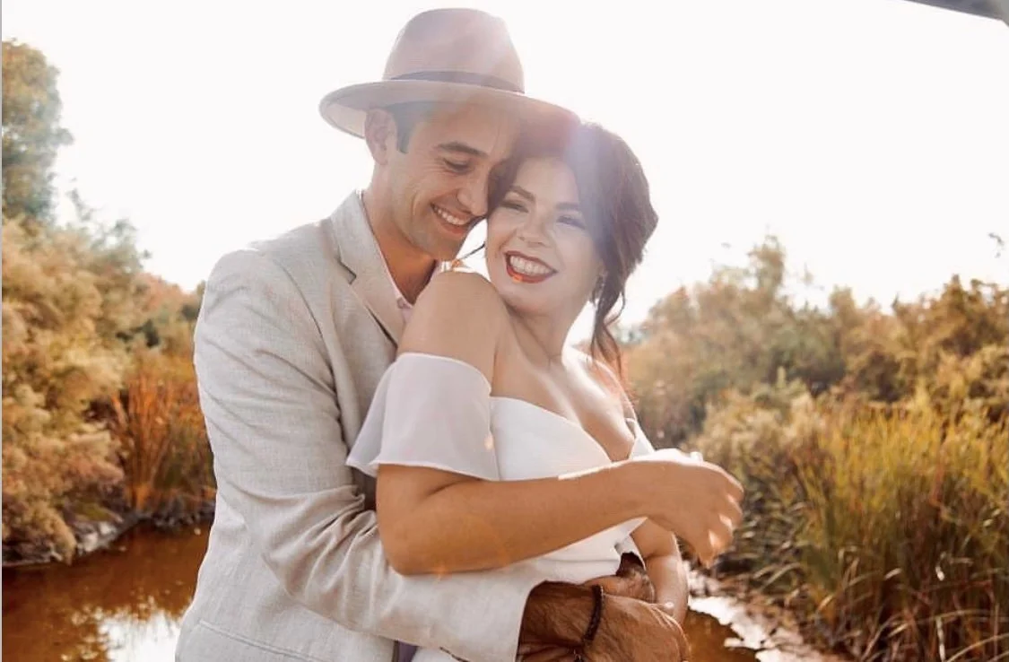 Bride with flawless, natural glam makeup embracing her partner, glowing with confidence and timeless, elevated bridal beauty