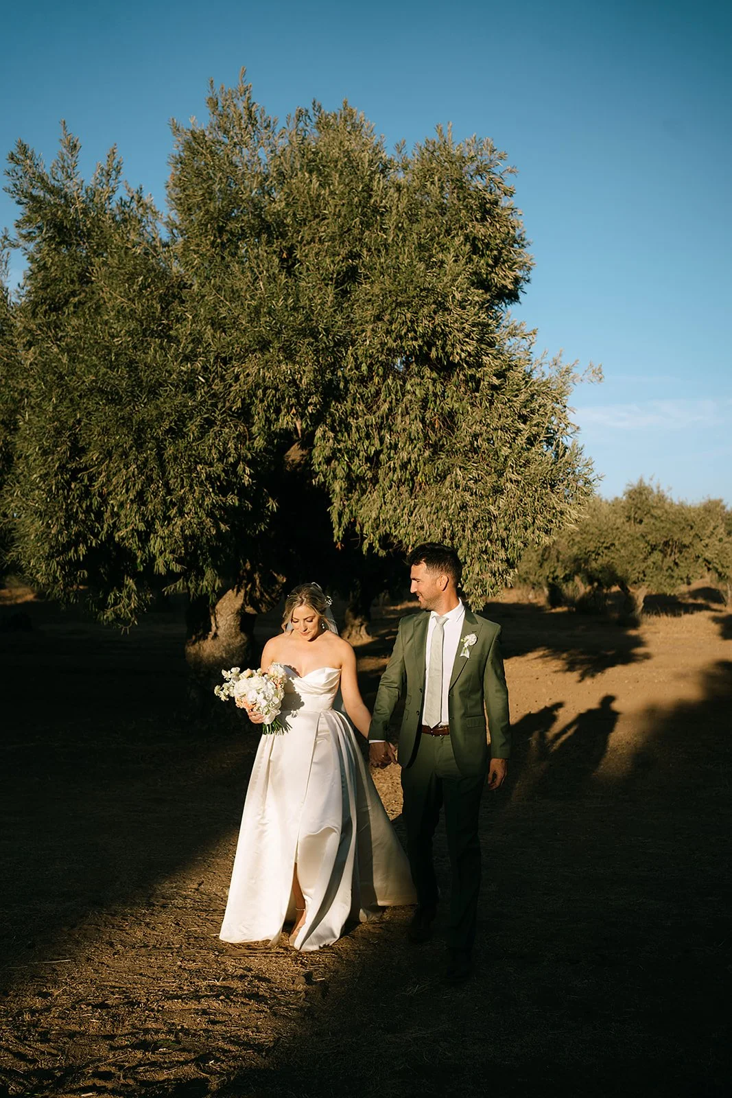Bride with glowing, natural glam makeup walking hand in hand with her partner at sunset, radiating confidence and effortless bridal beauty