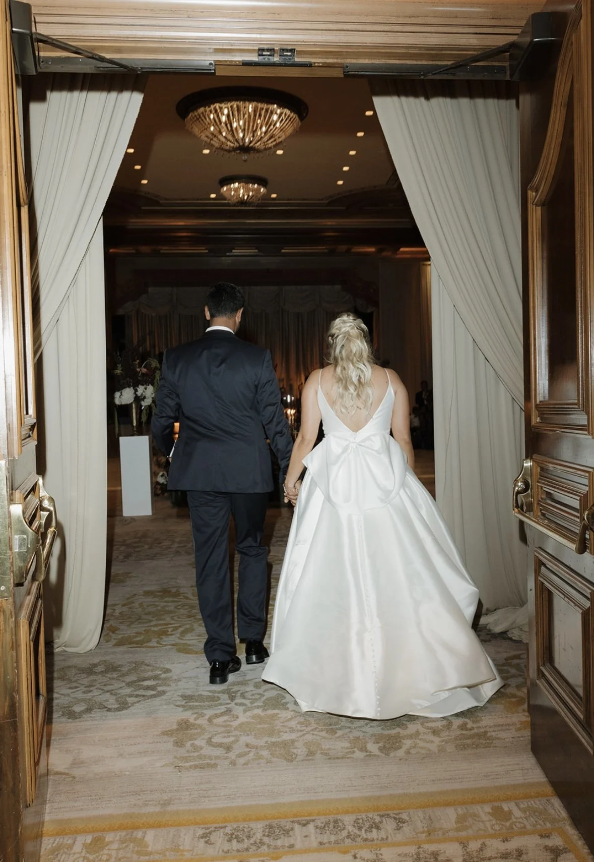 Bride with soft, timeless bridal glam walking confidently with her partner into their reception, looking radiant and effortlessly elegant