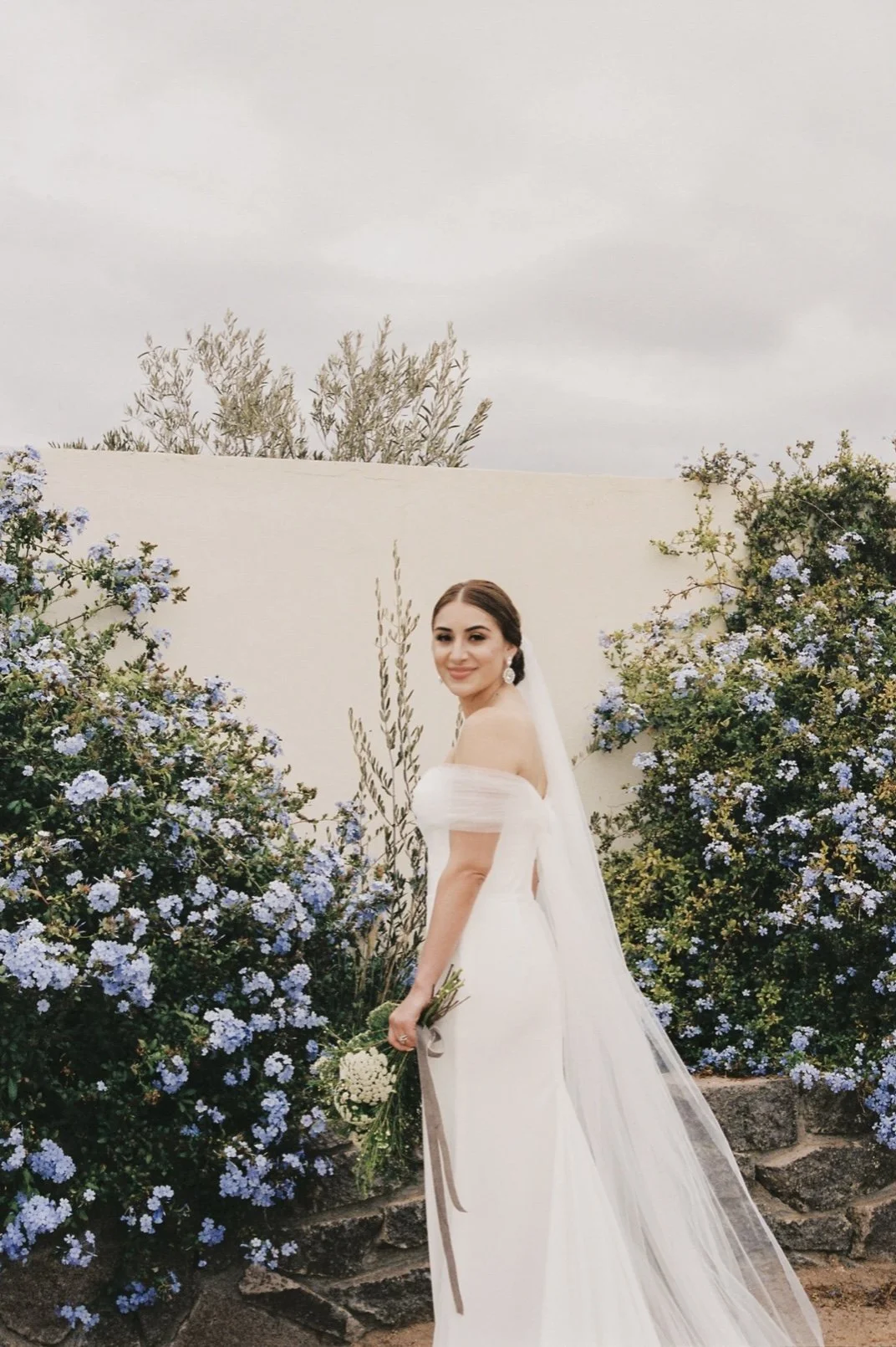 Bride with natural glam makeup holding her bouquet outdoors, looking confident, radiant, and camera-ready in Valle de Guadalupe Baja CA MX