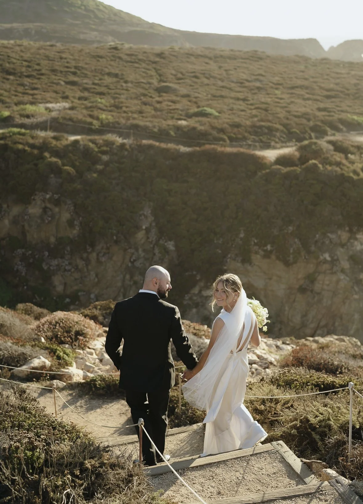 Bride with soft, natural glam makeup and romantic hairstyle walking confidently with her partner in an outdoor wedding setting