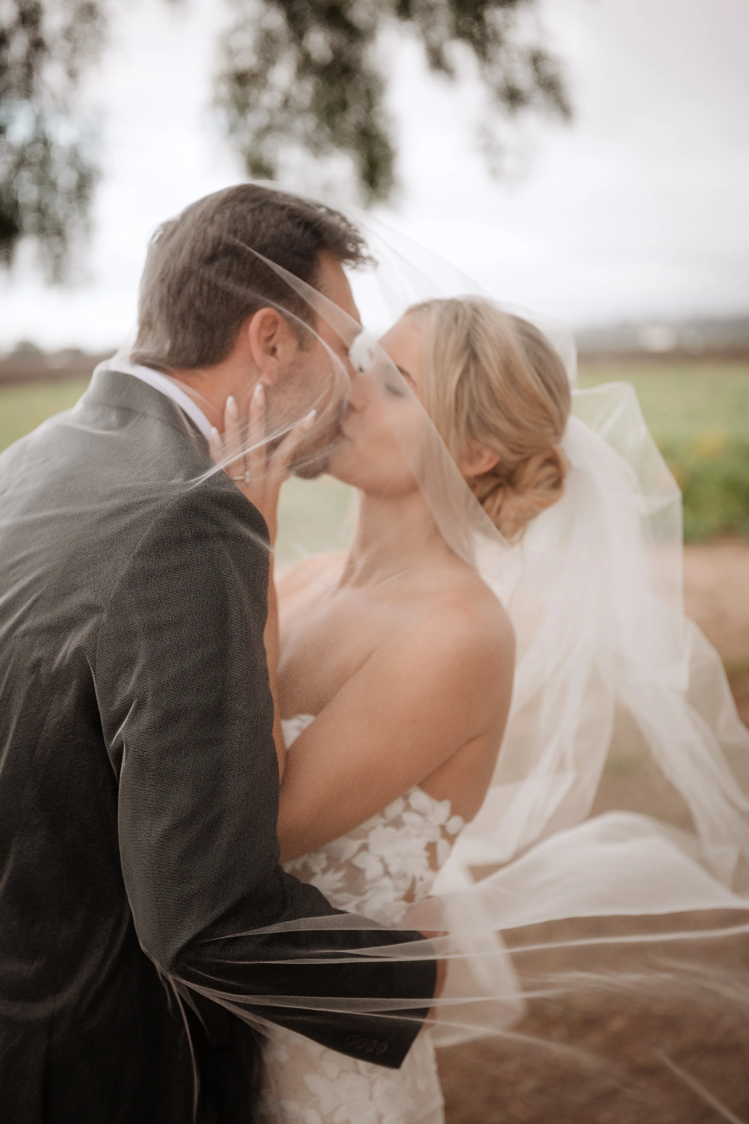Bride with radiant, soft glam makeup sharing a romantic veil moment with her partner, looking confident and timeless