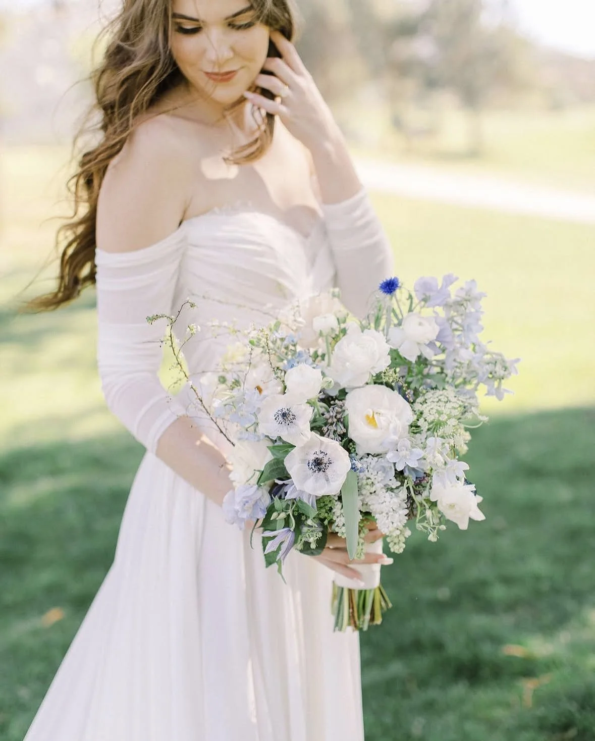 Bride with soft, natural glam makeup and romantic bridal hairstyle holding bouquet during an outdoor wedding