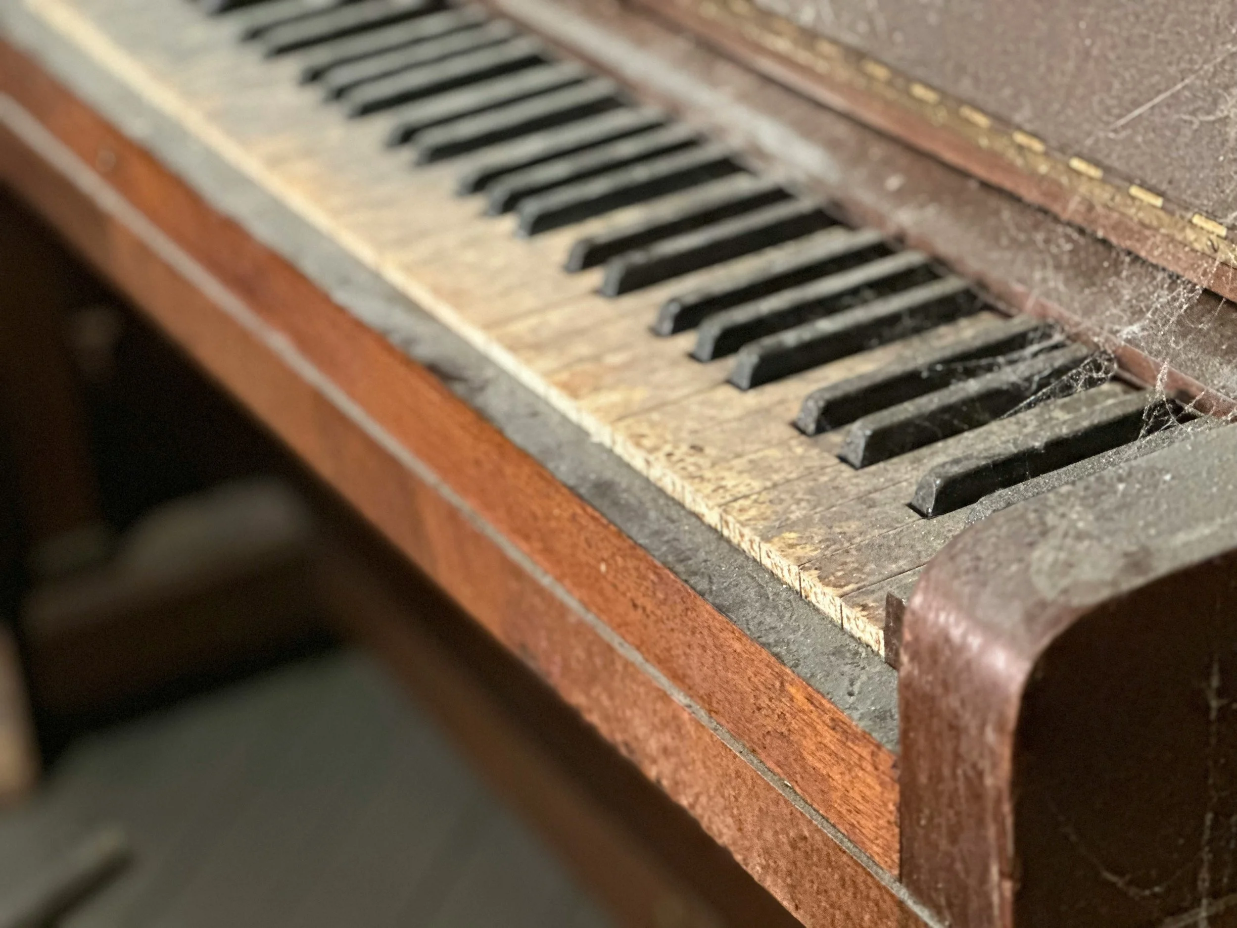 Close-up of an old, dusty piano keyboard with worn keys and cobwebs.