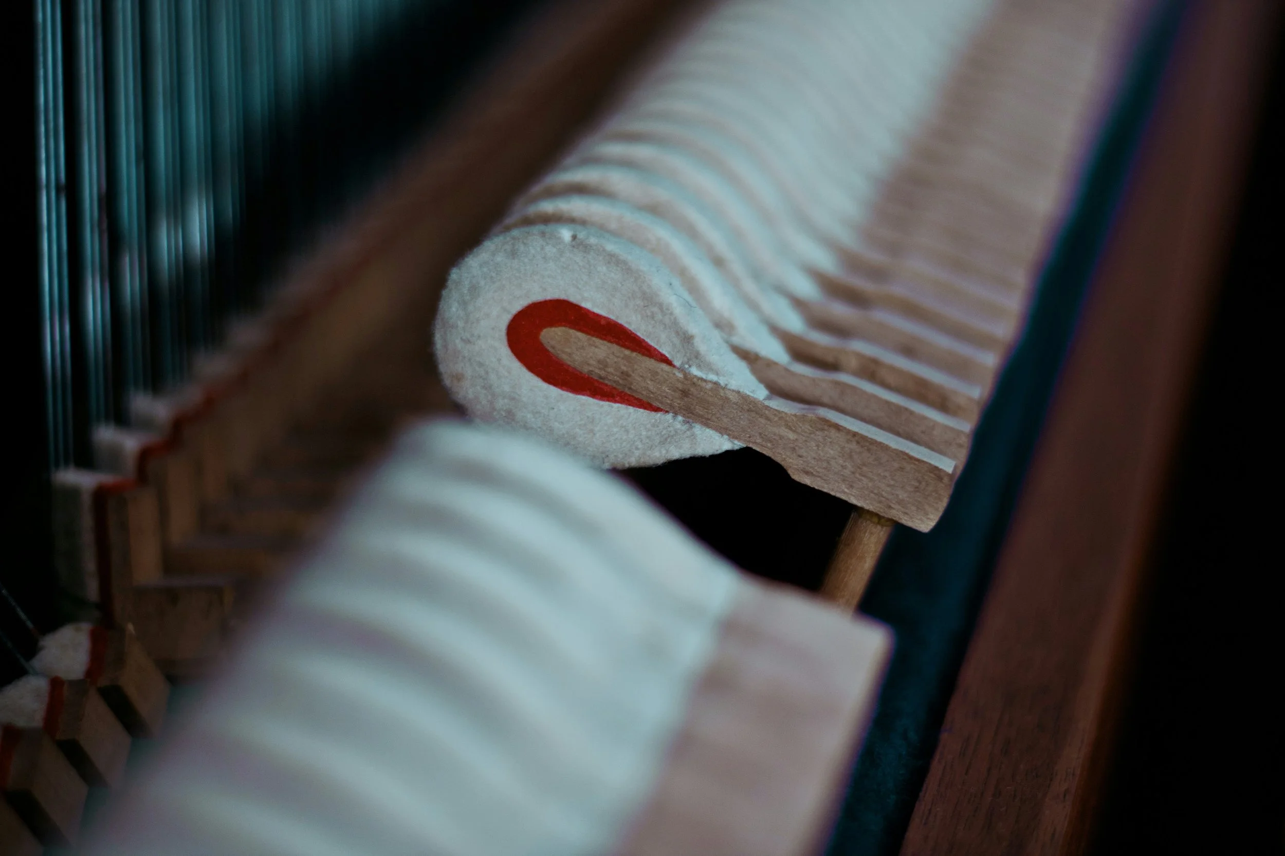 Close-up of piano hammers, focusing on one with a red marking, inside a piano.
