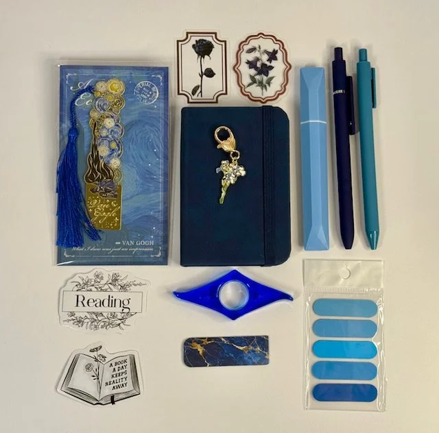 Flat lay of stationery and accessories, including pens, sticky notes, bookmarks, a notebook with keychain, decorative stickers, a hair tie bracelet, and books.