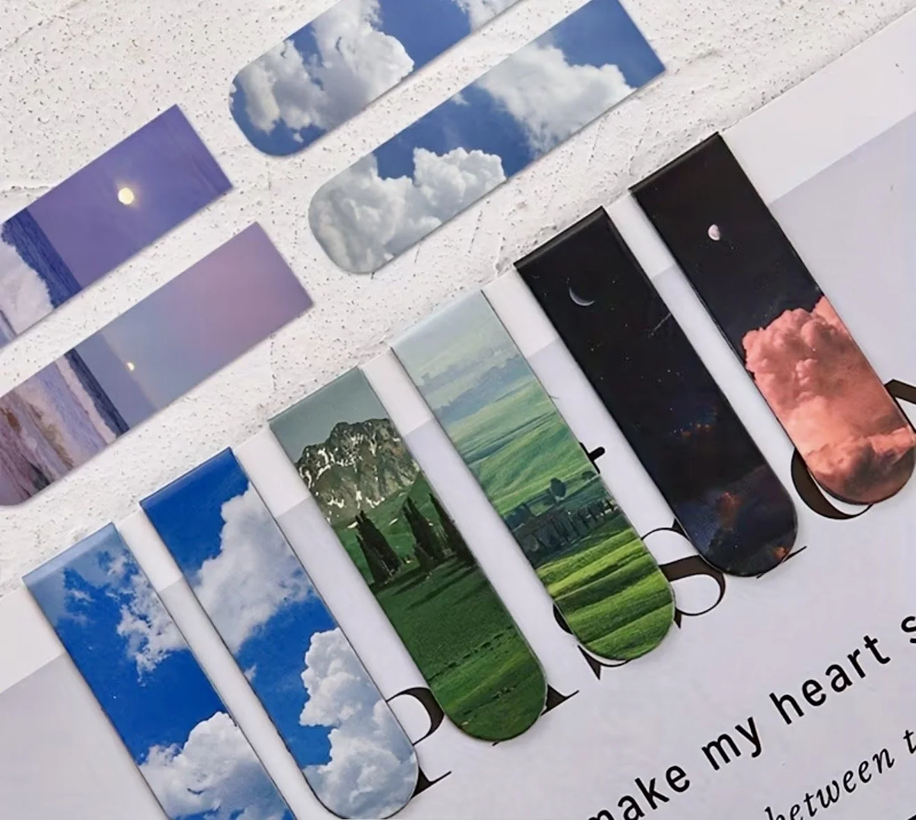 Collection of magnetic bookmarks with various sky and landscape designs laid out on a white surface.