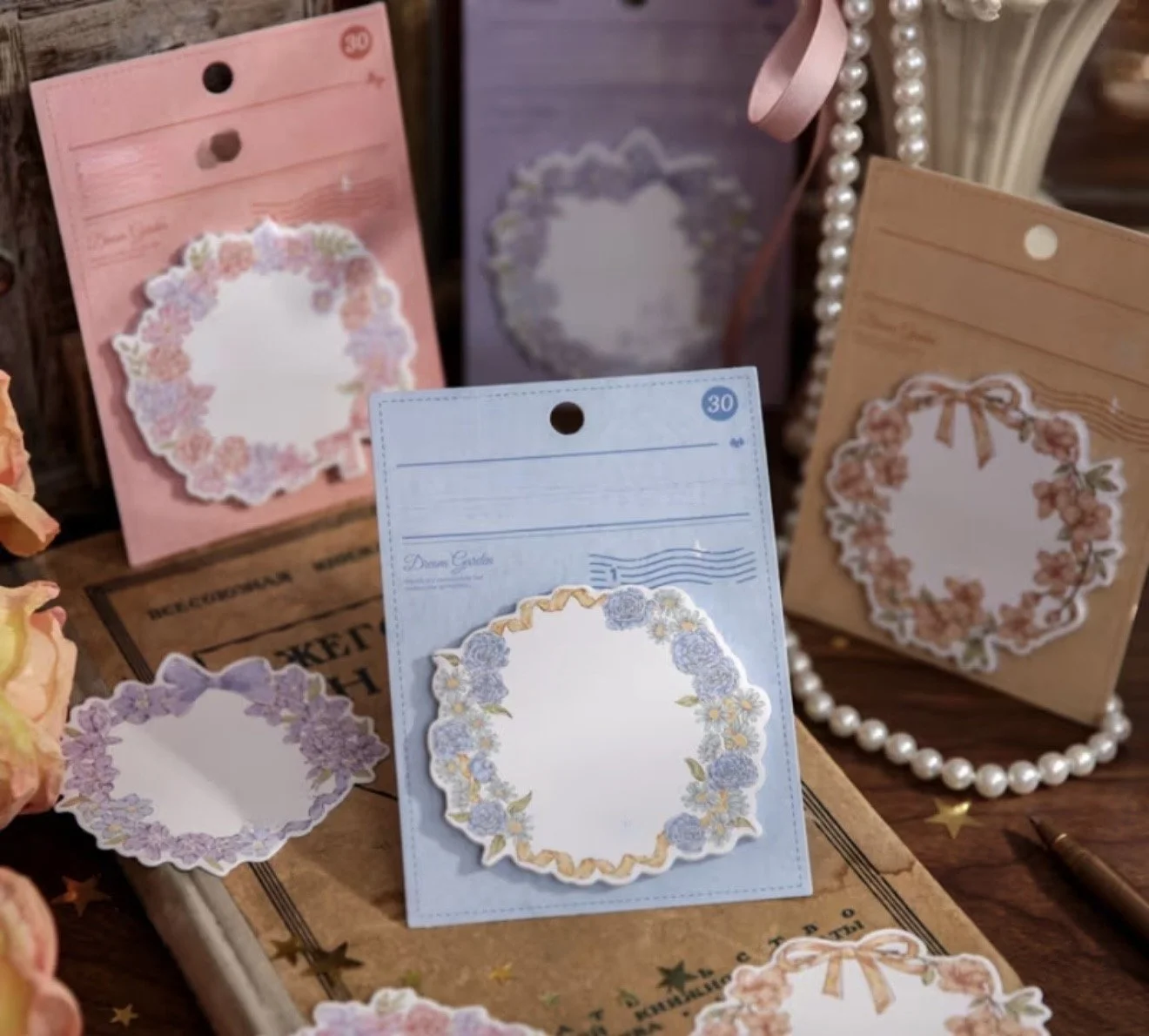 Decorative floral stationery cards with envelopes and background accessories, including a string of pearls and a box of paper notes.
