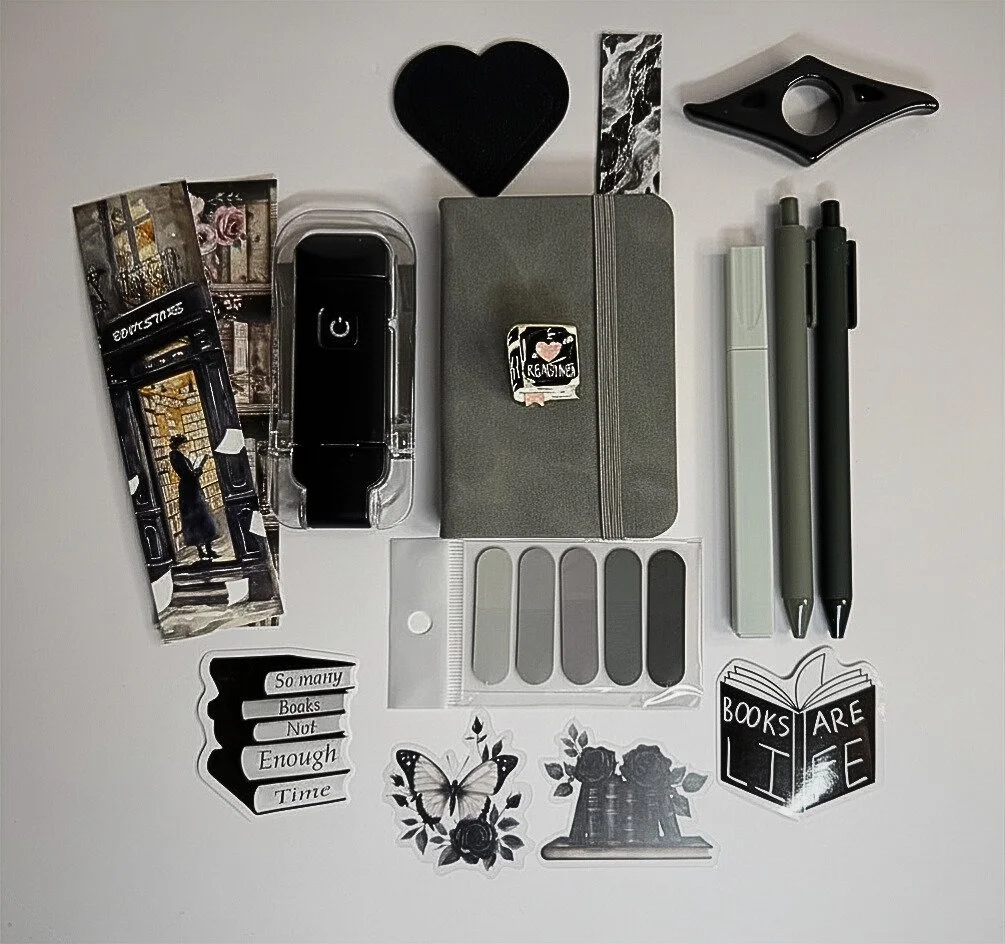 Flat lay of various stationery and decorative items, including pens, stickers, a notebook, a phone, and small decorative pieces.