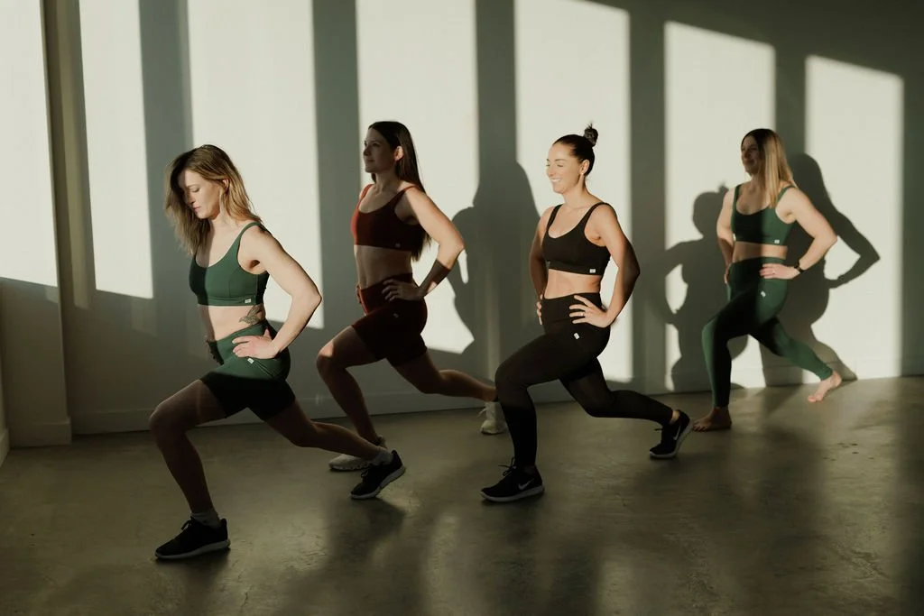 Four women doing yoga in a studio with sunlight and shadows on the wall.