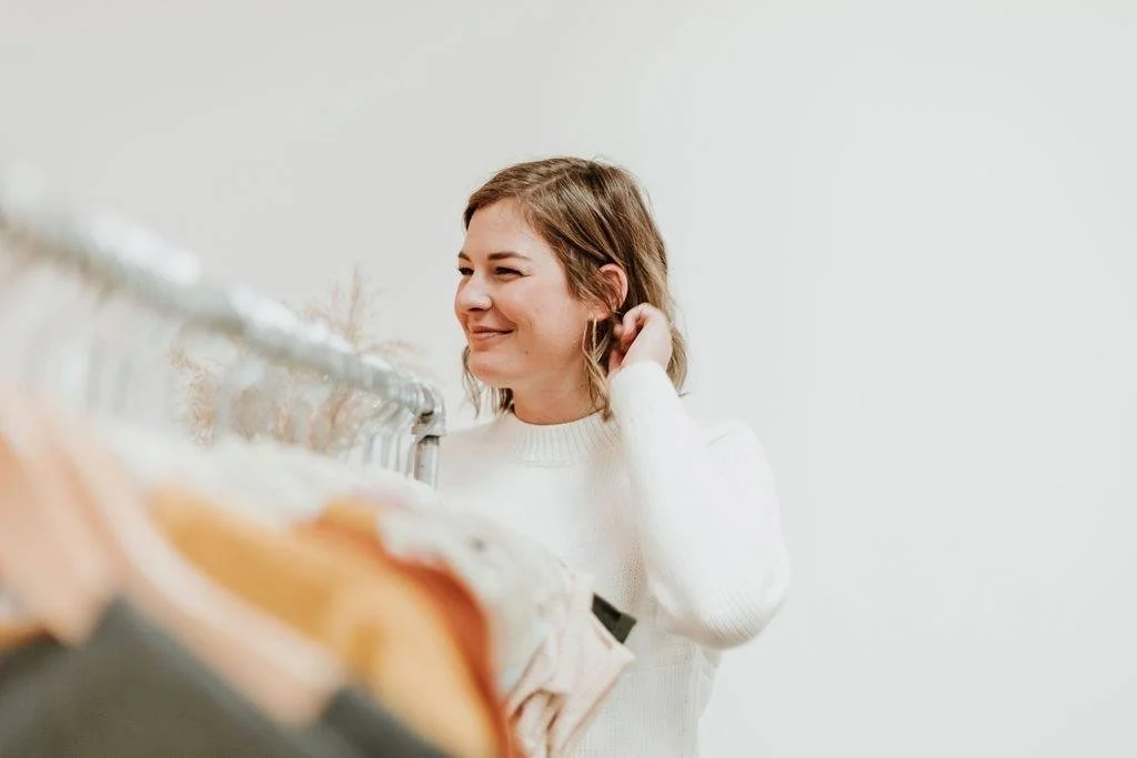 A woman shopping for clothes in a store, looking at a clothing rack with a smile.