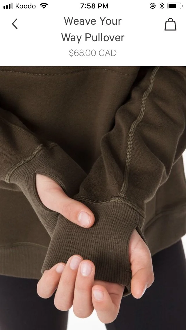 Person wearing a brown hoodie with a pocket, holding the sleeve with their other hand, showing the cuff and zipper detail.