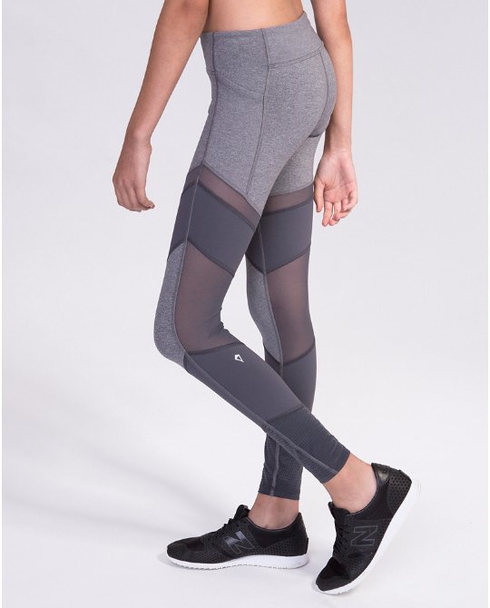 A woman wearing gray athletic leggings with mesh panels and black sneakers, standing against a plain background.