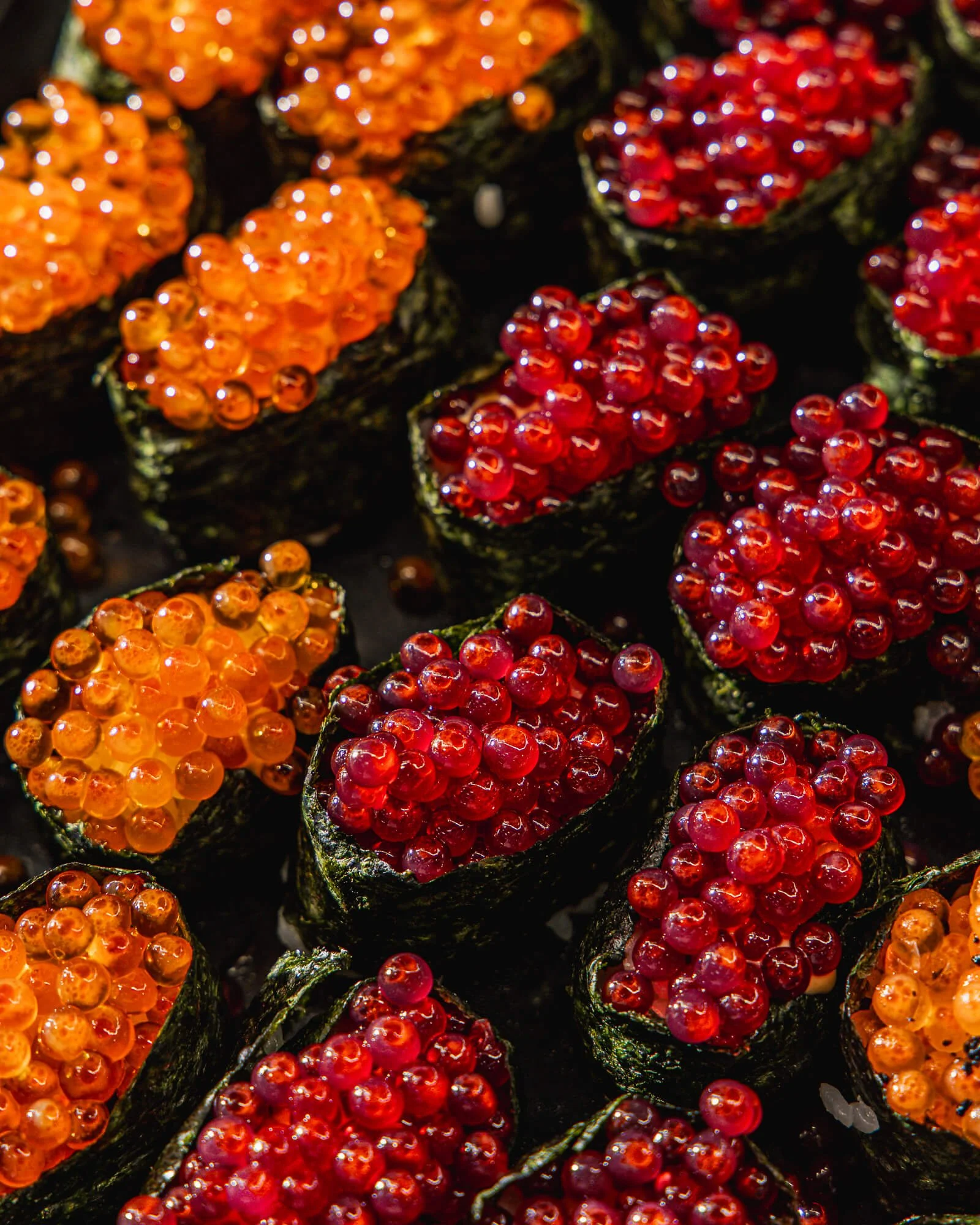 Close-up of multiple sushi rolls topped with orange and red fish roe.