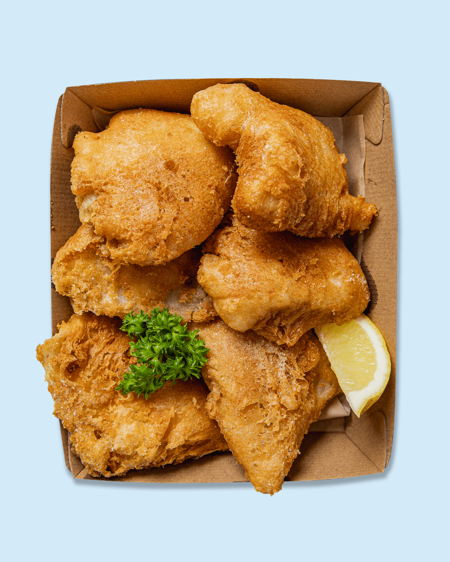 Fried chicken tenders with a lemon wedge and parsley on a paper-lined tray, with a restaurant branding visible.