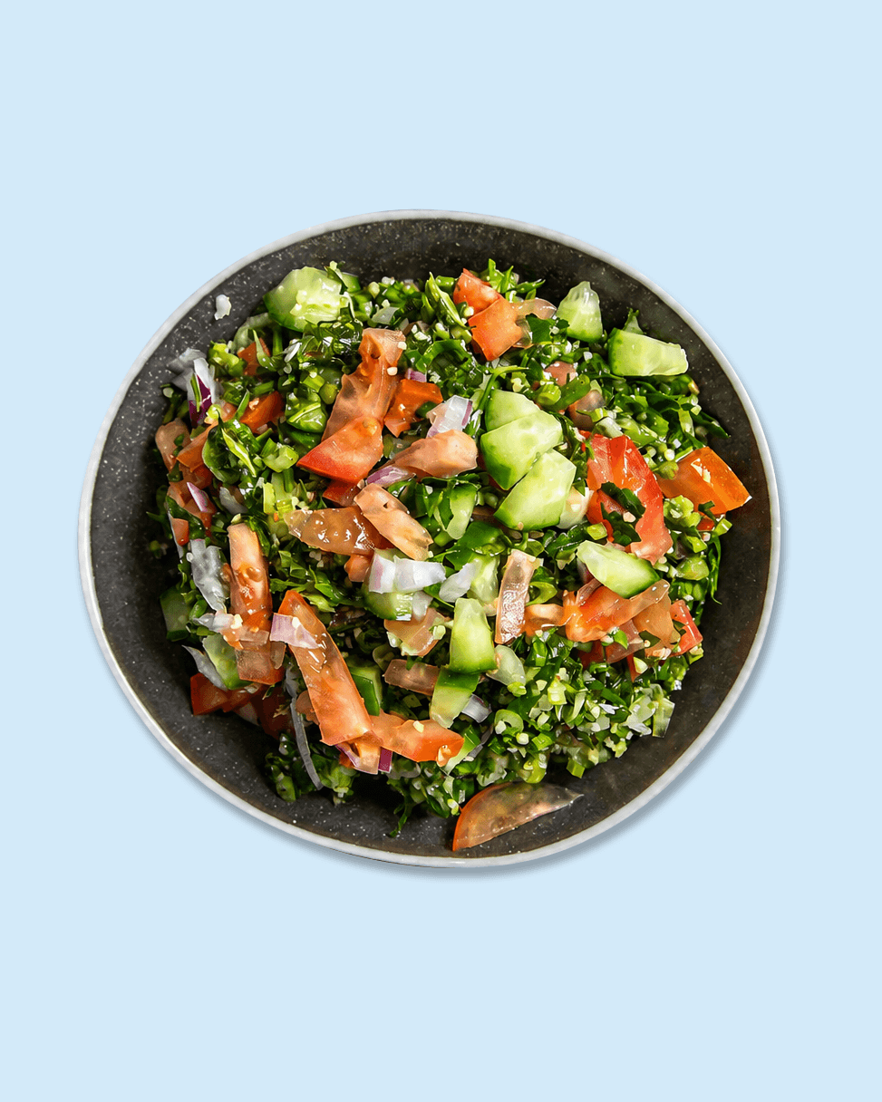 A bowl of chopped salad with cucumbers, tomatoes, onions, and greens on a paper liner with 'Nicholas' logo.