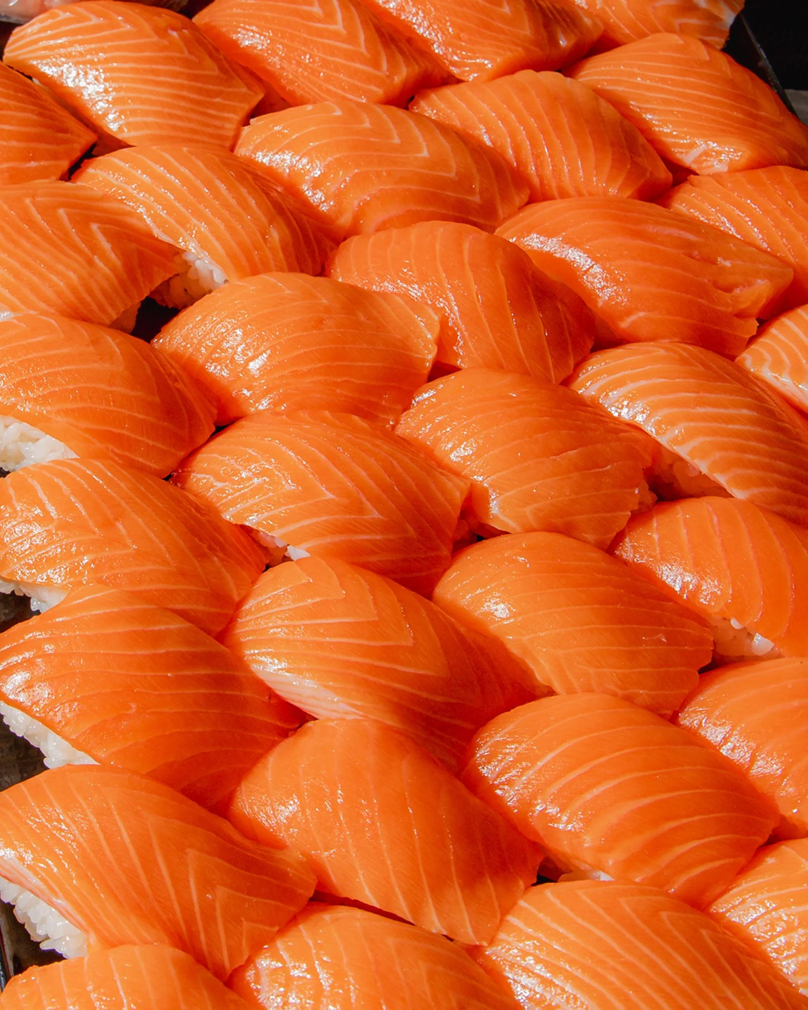 Multiple pieces of fresh salmon sashimi with visible orange flesh and white marbling, arranged on a dark surface.