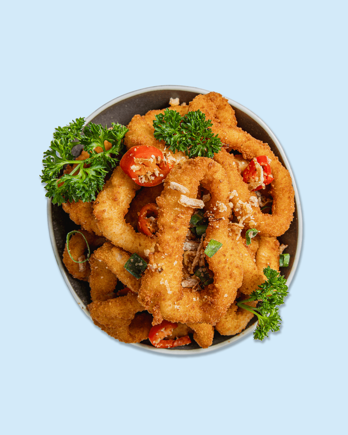 Close-up of fried onion rings garnished with parsley and chopped red pepper, served on a plate.