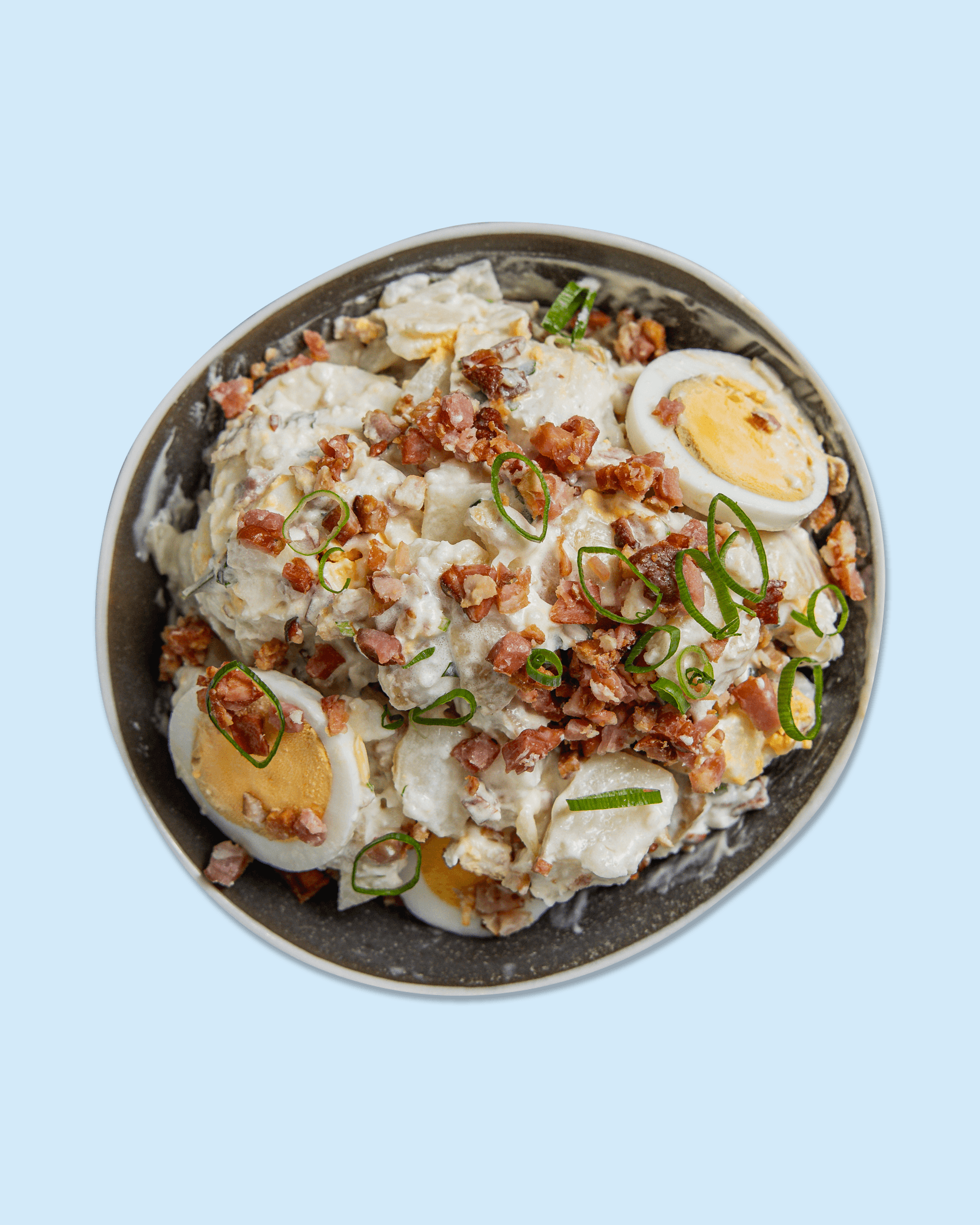 Salad with sliced eggs, chopped bacon, green onions, and creamy dressing, served in a bowl on branded paper.