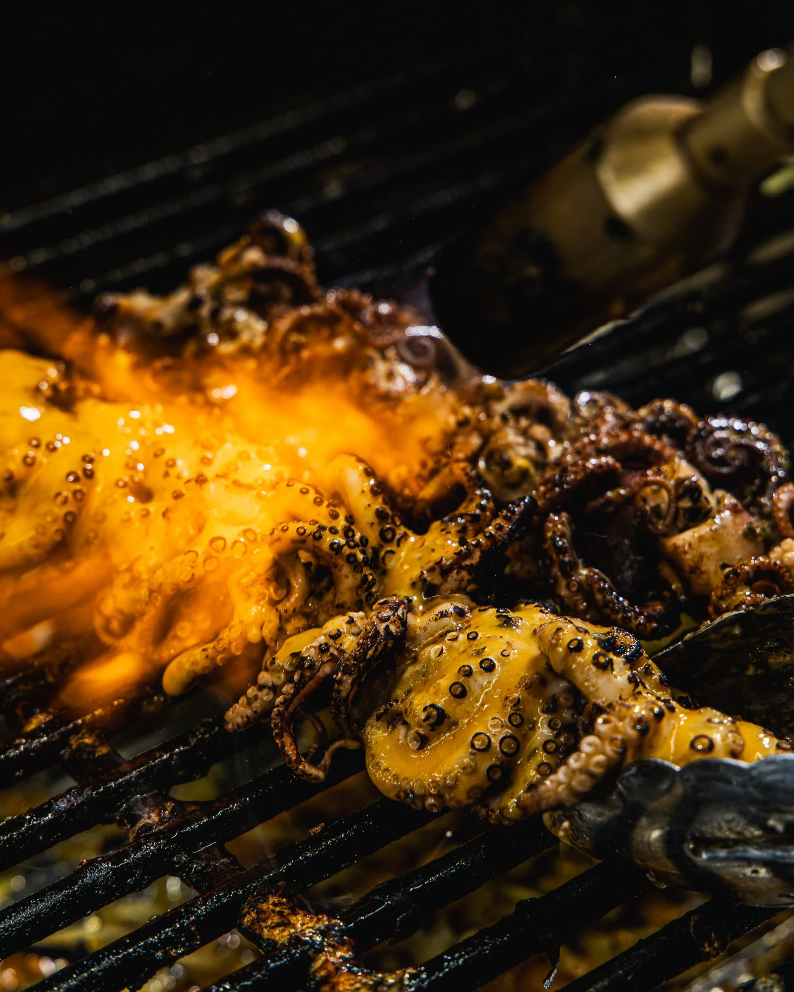 Close-up of grilled octopus tentacles on a barbecue grill with some charred spots and juices.