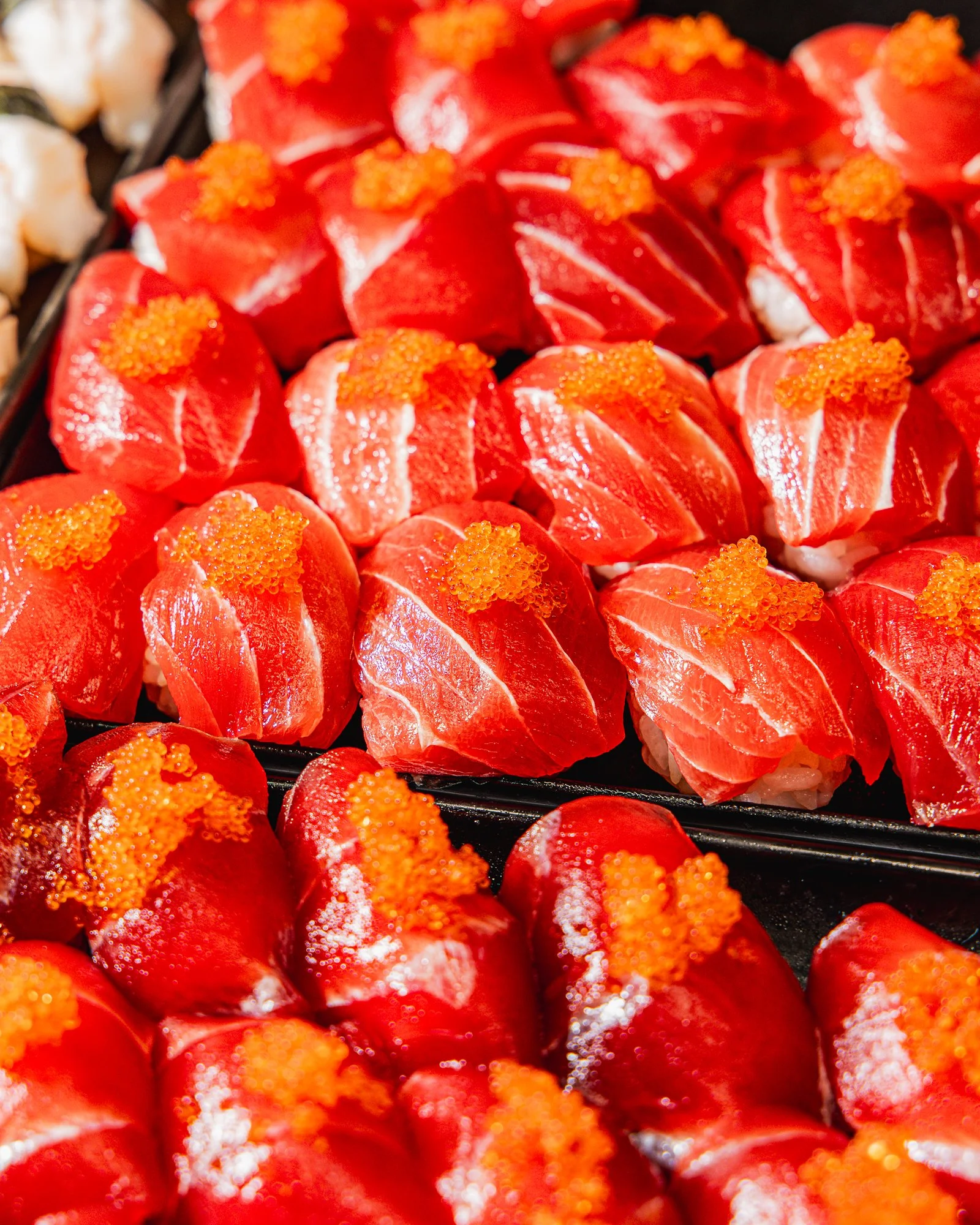 Close-up view of multiple pieces of sushi with bright red fish, topped with orange fish roe.