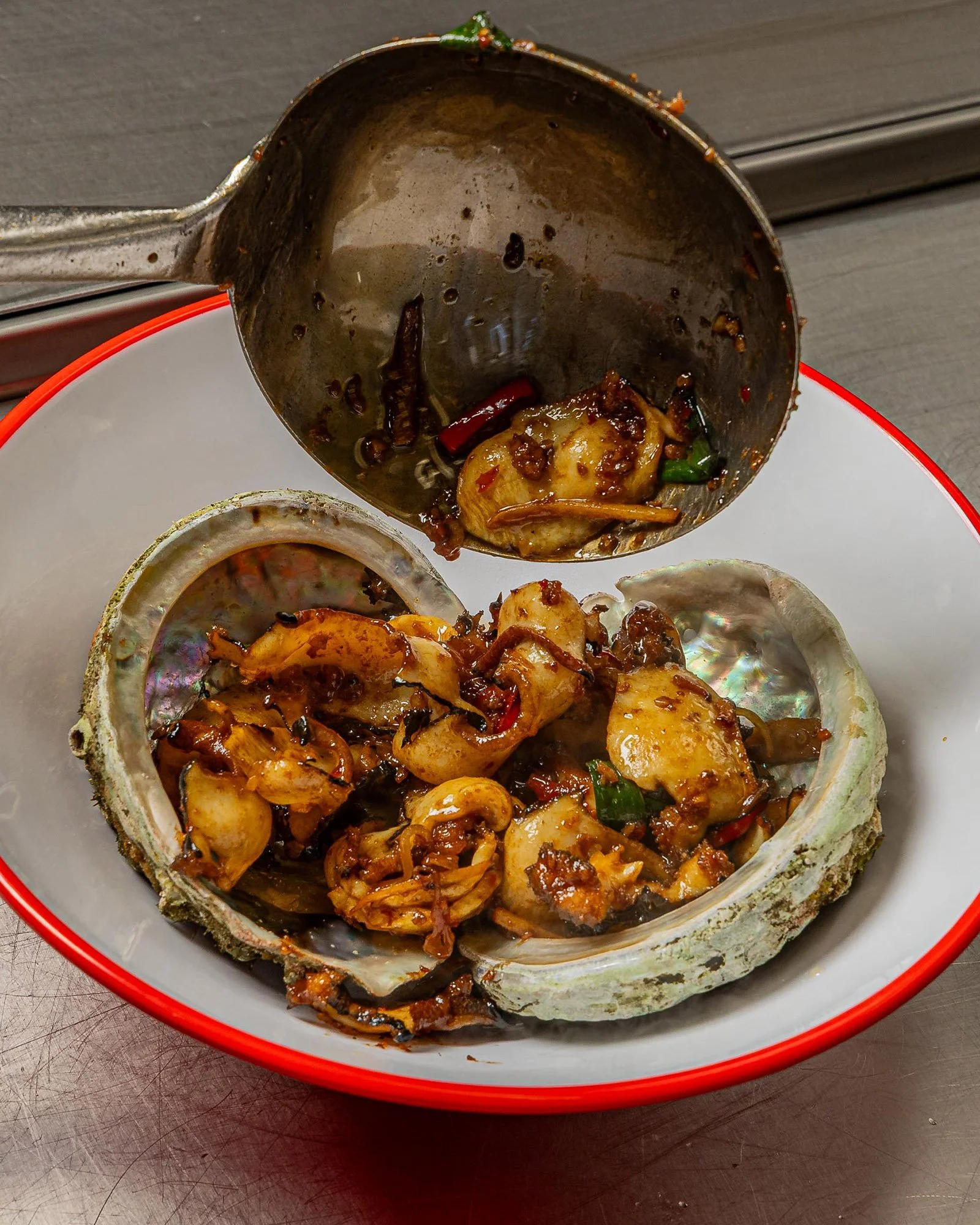 Empty oyster shell filled with cooked seafood and spicy sauce, placed inside a red-rimmed bowl.