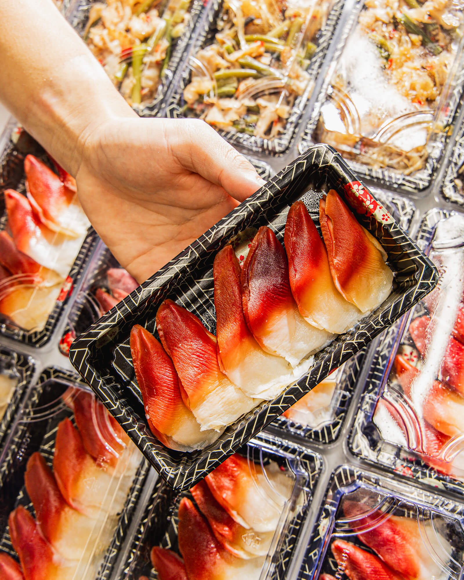 Close-up of packaged raw fish fillets in a black and gold patterned container, with various other fish fillets visible in the background.