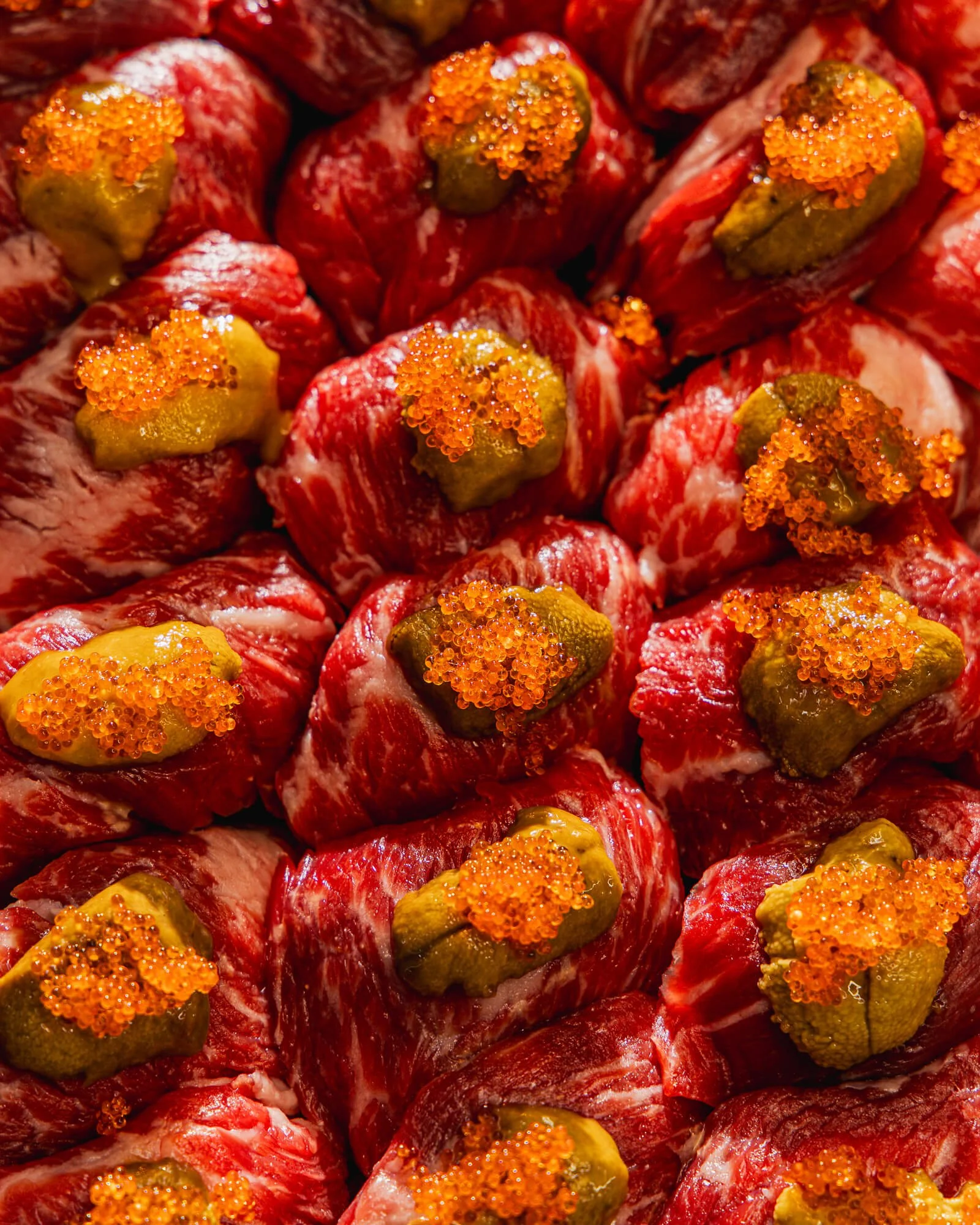 Close-up of raw red meat pieces topped with green and orange roe roe