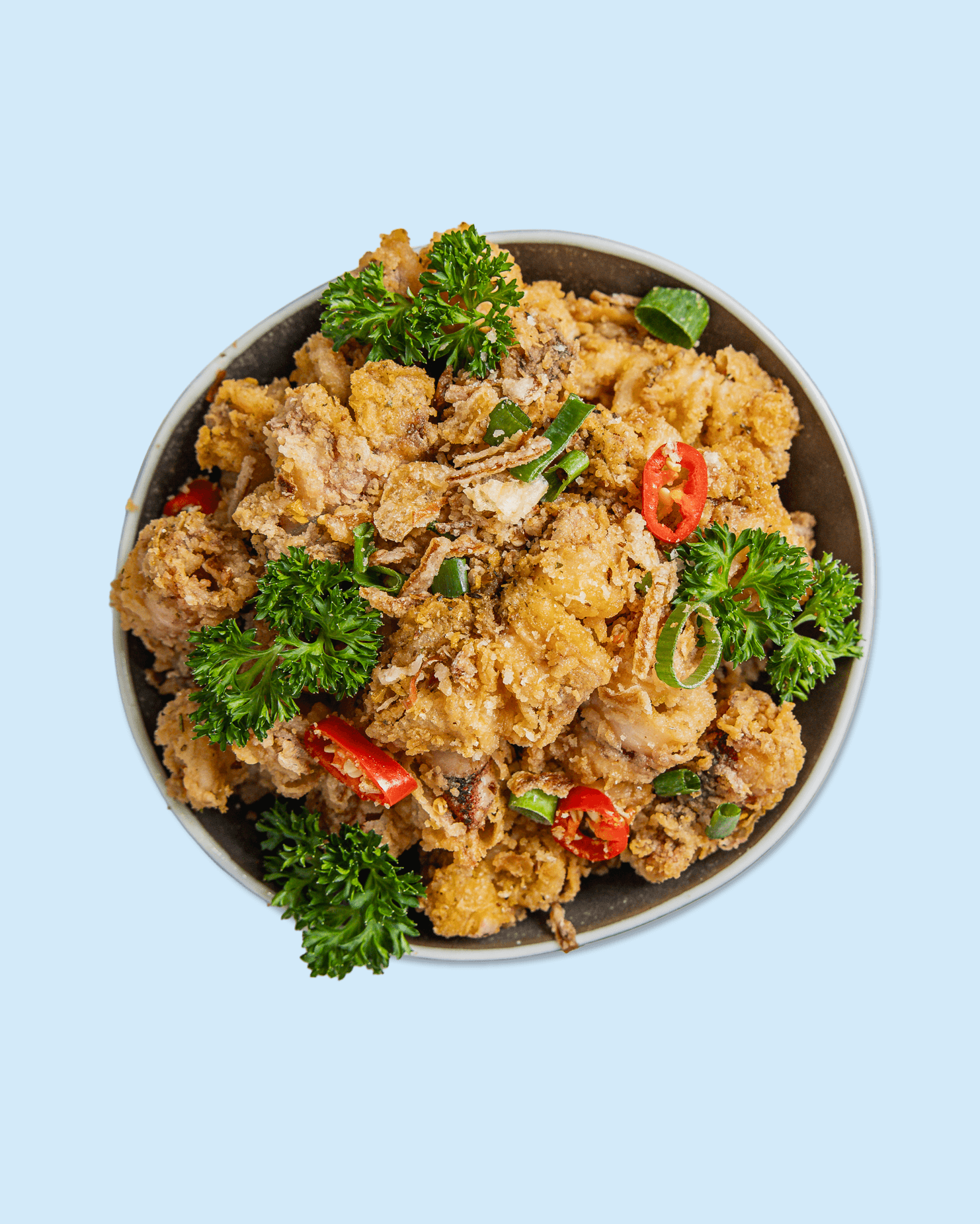 Fried chicken with red chili slices and parsley on a plate.