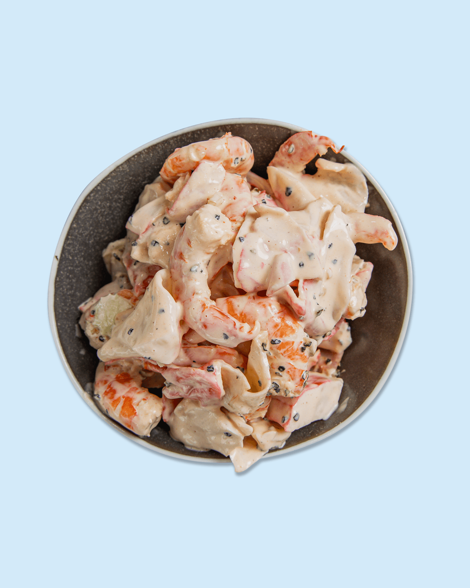 A bowl of potato salad with mayonnaise, carrots, black pepper, and other ingredients on branded paper.