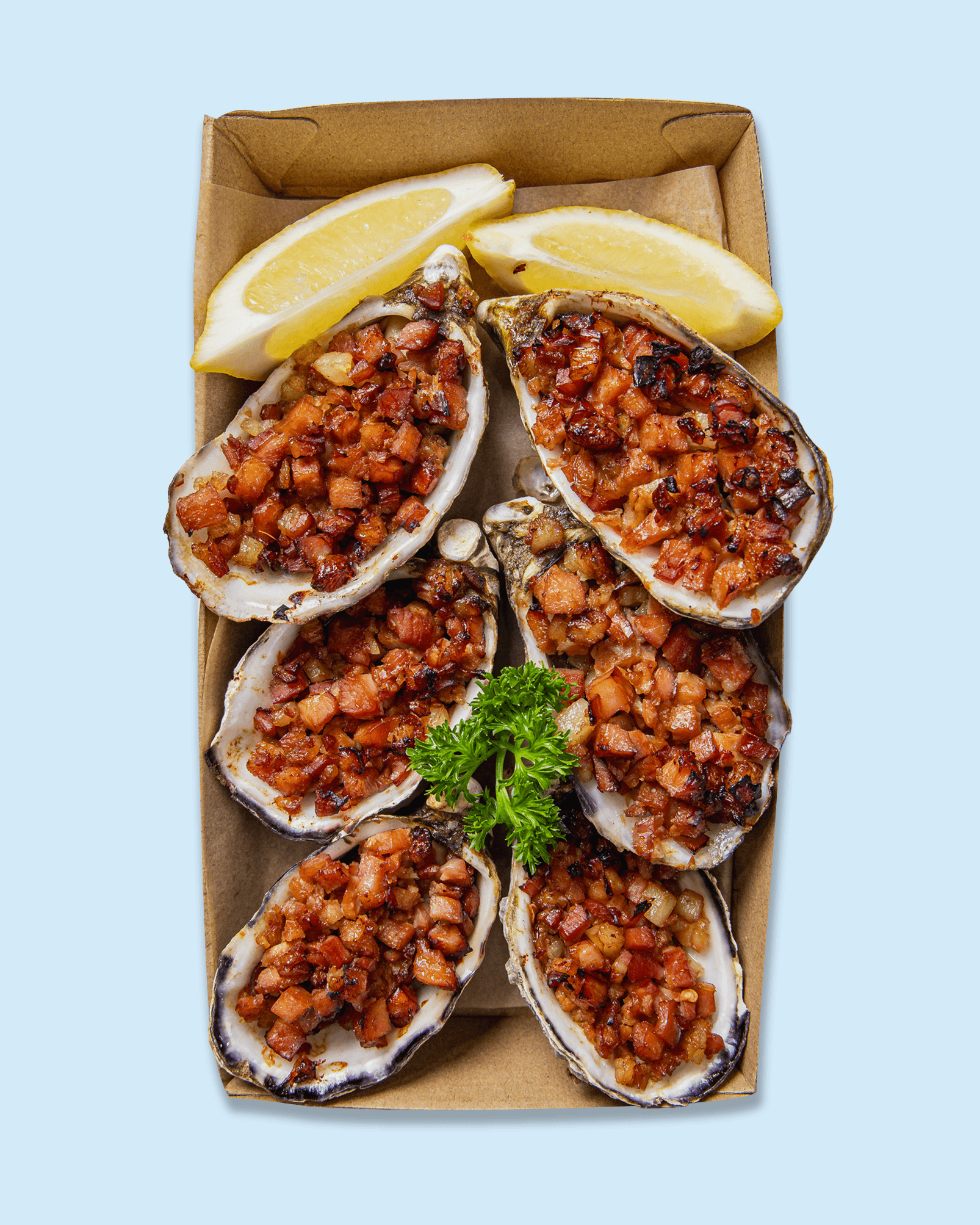 Close-up of baked oysters topped with diced bacon, served with lemon wedges and garnished with parsley.