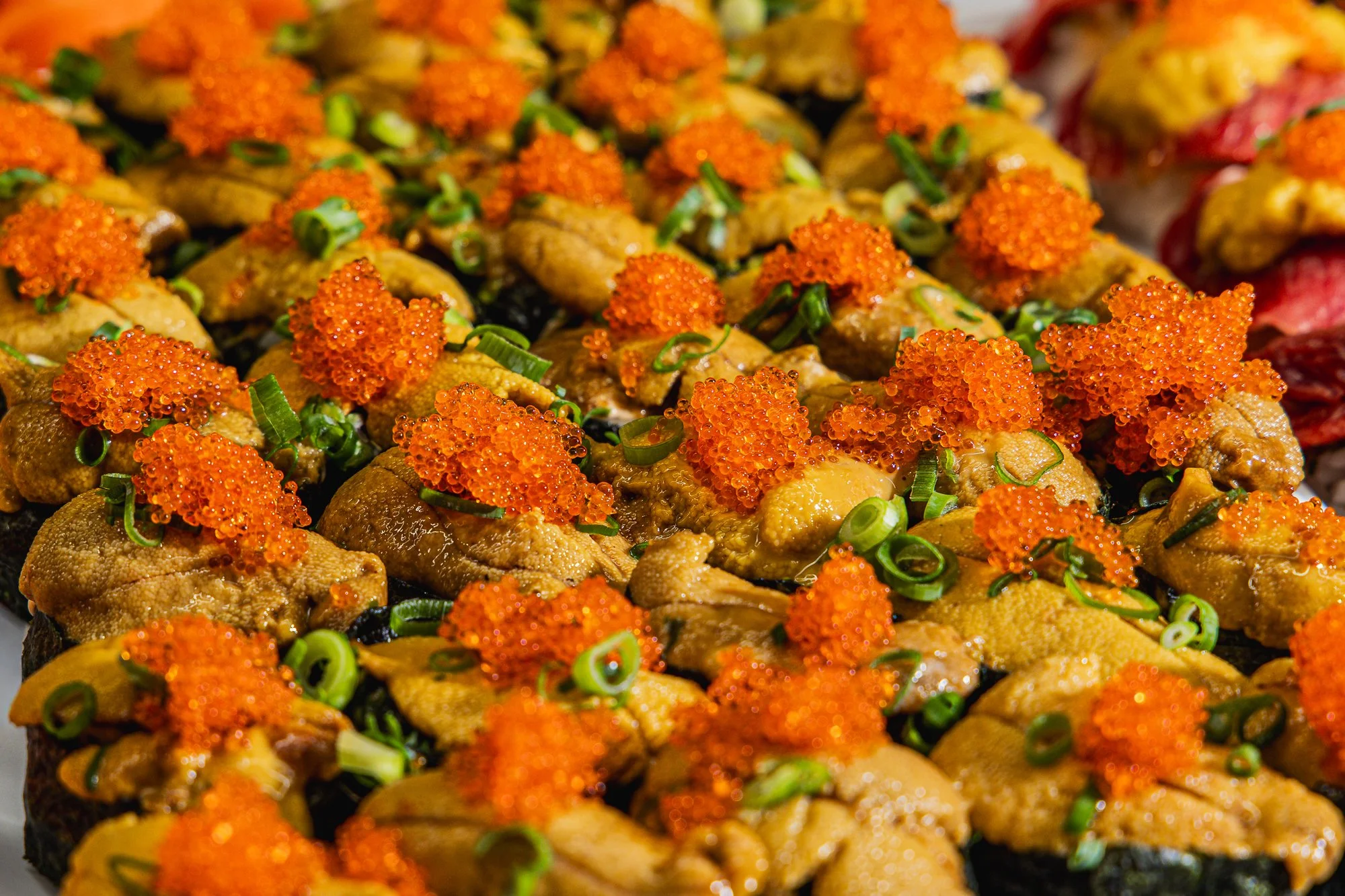 Close-up of sushi topped with orange fish roe and chopped green onions.