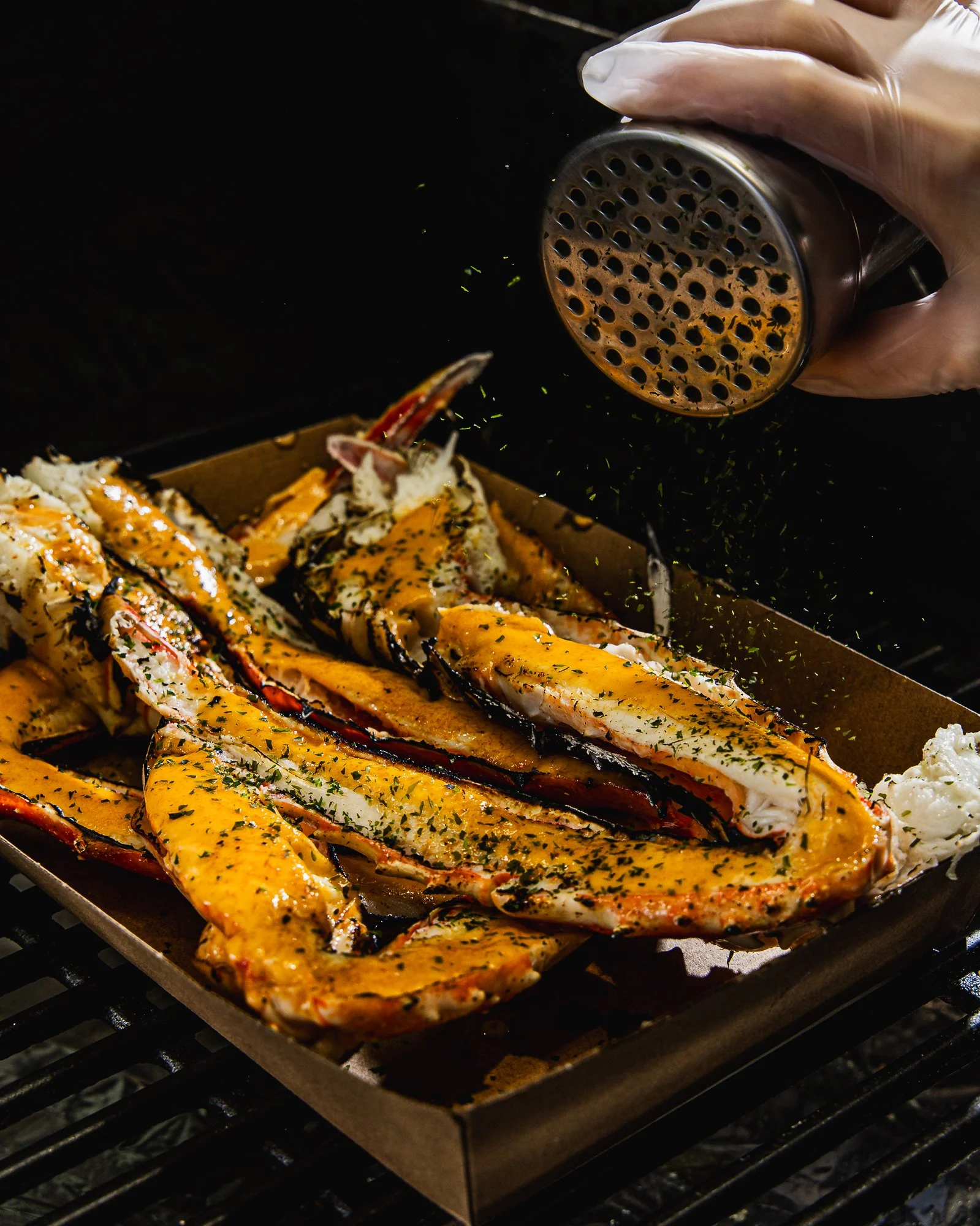 Grilled lobster tails with melted butter, garnished with herbs, on a baking sheet in an outdoor grill.