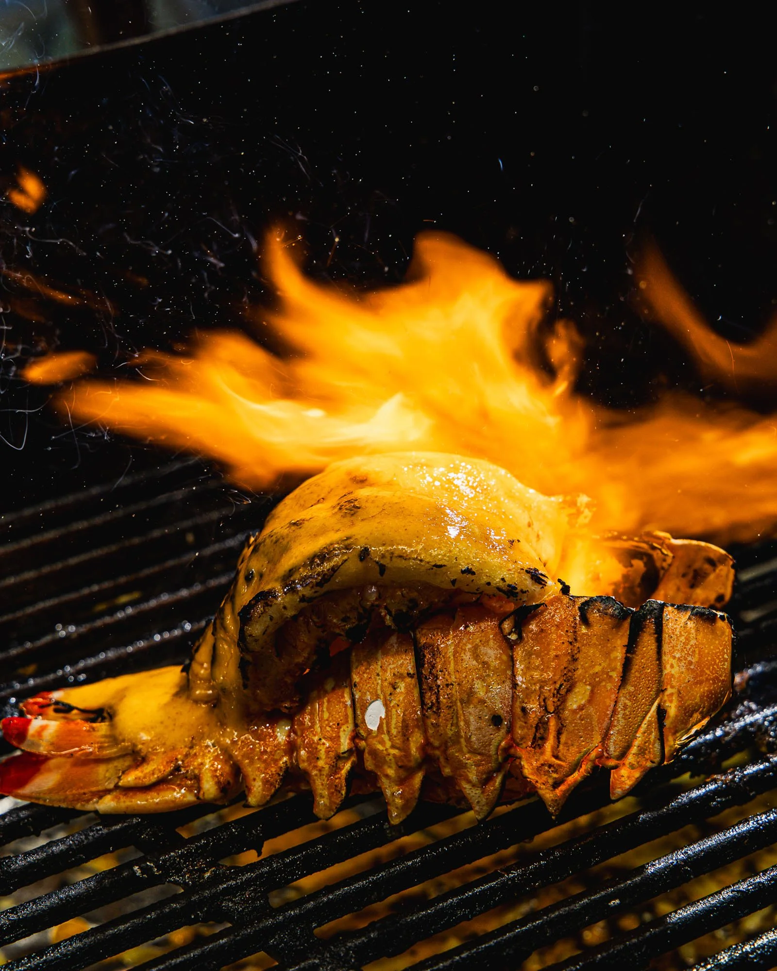 Lobster tail being grilled over flames.