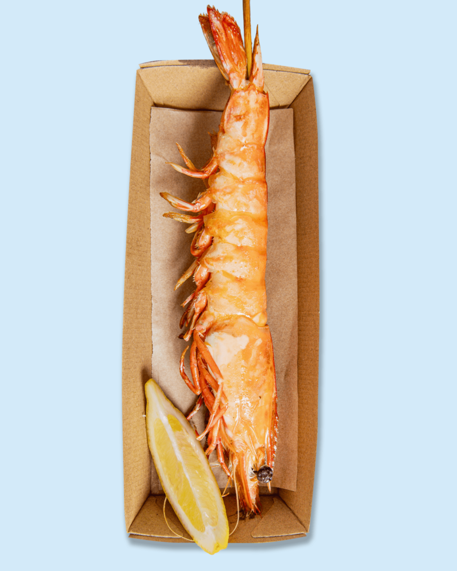 A cooked lobster tail with a lemon wedge on a paper-lined tray, on top of branded paper with 'NICHOLAS catering & events' printing.