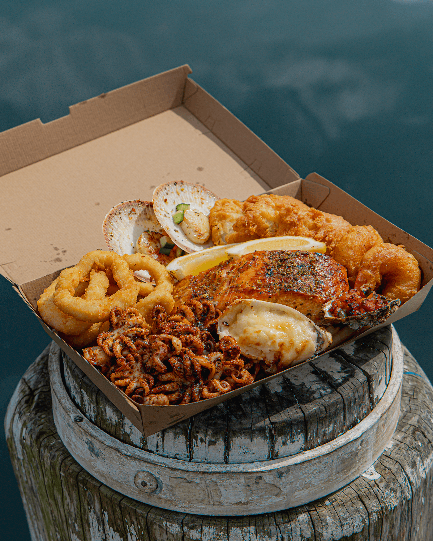 Variety of fried seafood including fish fillets, crab cakes, and stuffed shell, garnished with lemon wedges and green onions, served on a marble countertop.