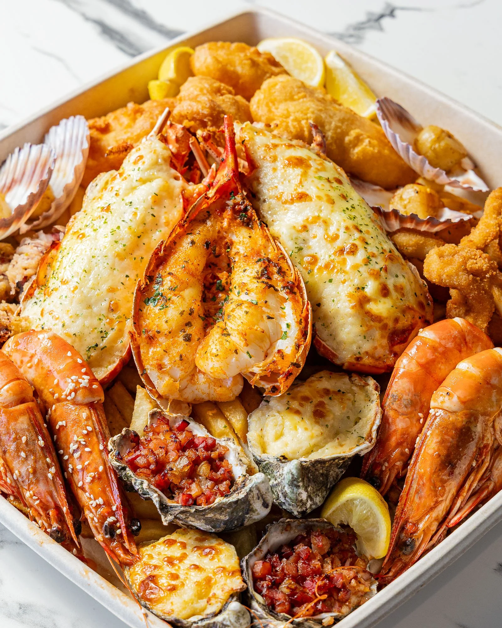 Seafood platter with lobster, shrimp, oysters, and crab, garnished with lemon wedges.