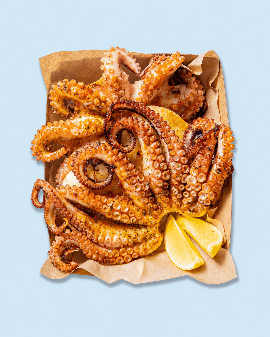 Close-up of cooked octopus tentacles served with lemon wedges on a white marble countertop.