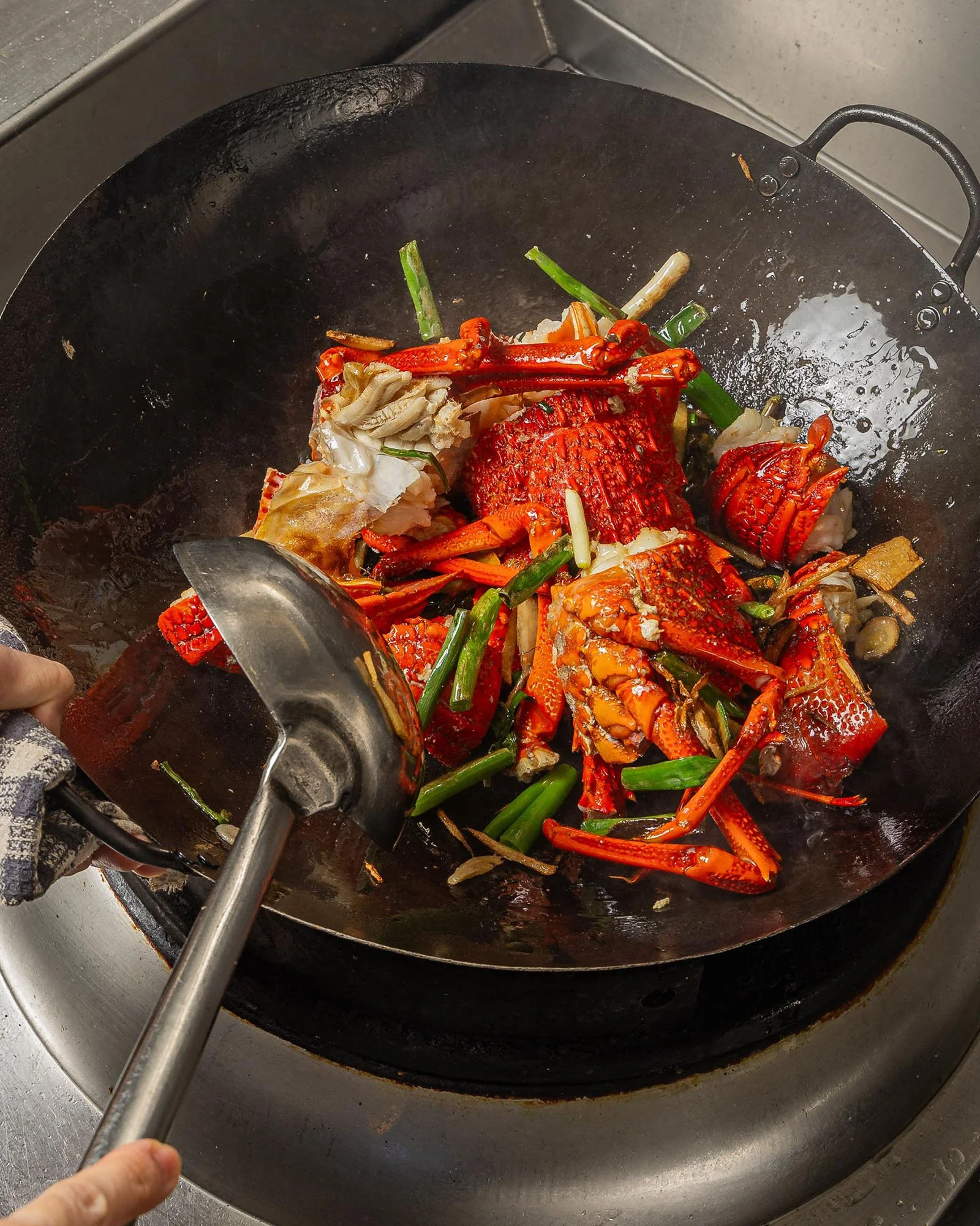 Cooking lobster with green onions in a wok, with a hand holding a spatula.
