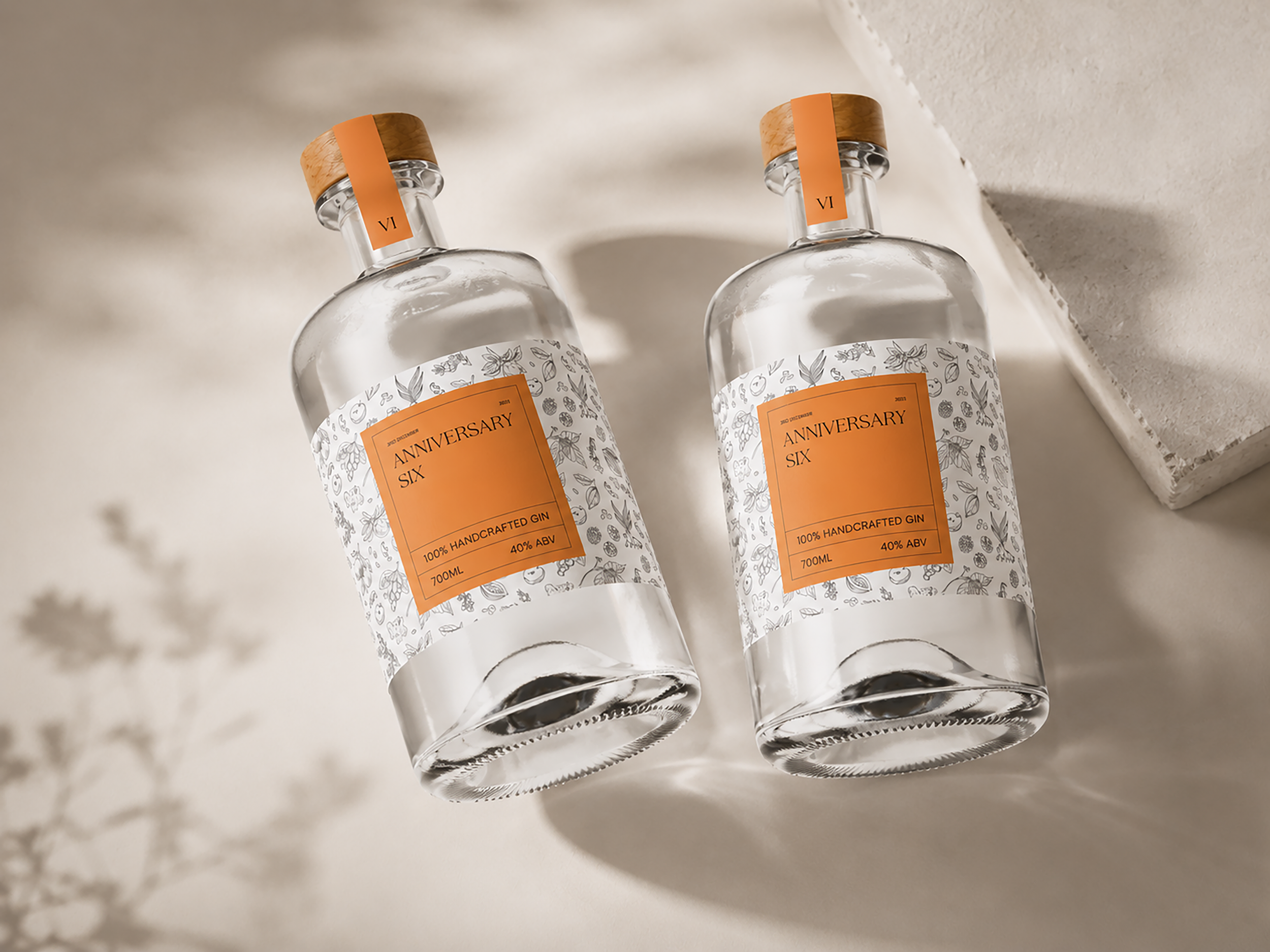 Two clear glass bottles labeled 'ANNIVERSARY SIX,' with orange and wooden cap seals, lying on a white surface with a light-colored textured background.
