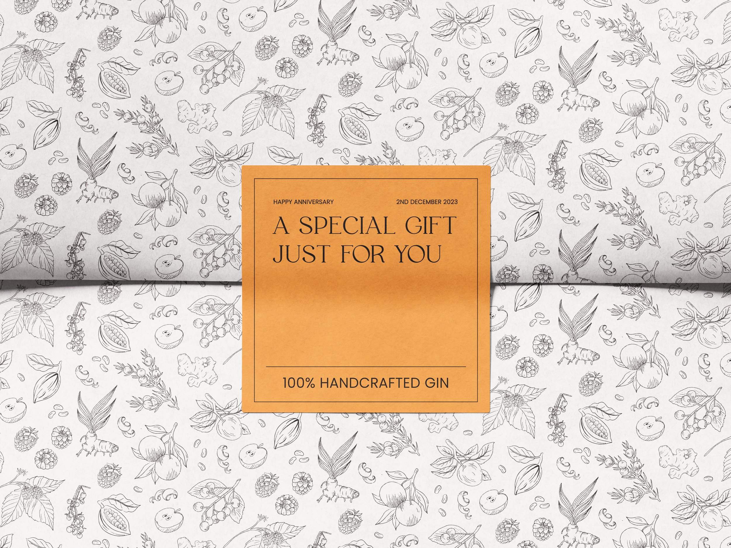 A gift box with a black and white fruit and herb pattern in the background. The box features an orange label with black text that reads 'Happy Anniversary, 2nd December 2023, A Special Gift Just for You, 100% Handcrafted Gin.'