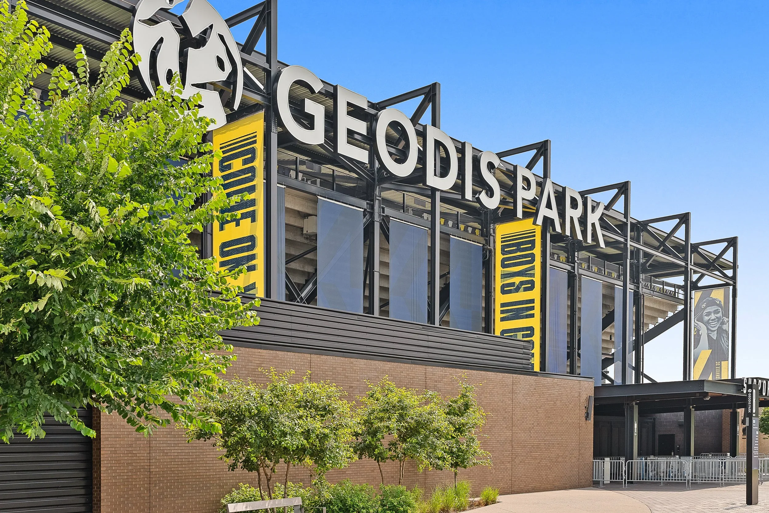 Exterior view of GEODIS Park stadium in Nashville with blue sky, green trees, and signage on the building.