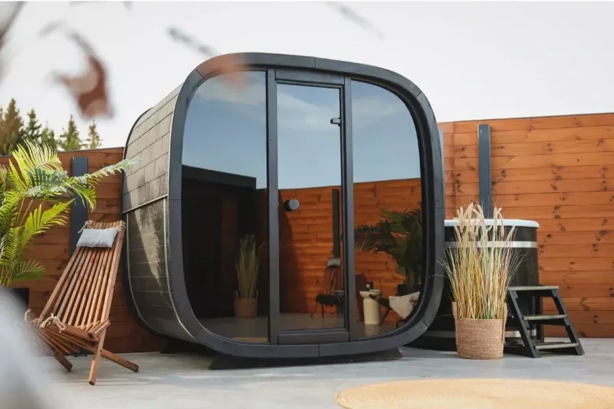 A modern outdoor hot tub or sauna with glass sliding door, surrounded by potted plants, a wooden deck, and a wooden privacy fence.