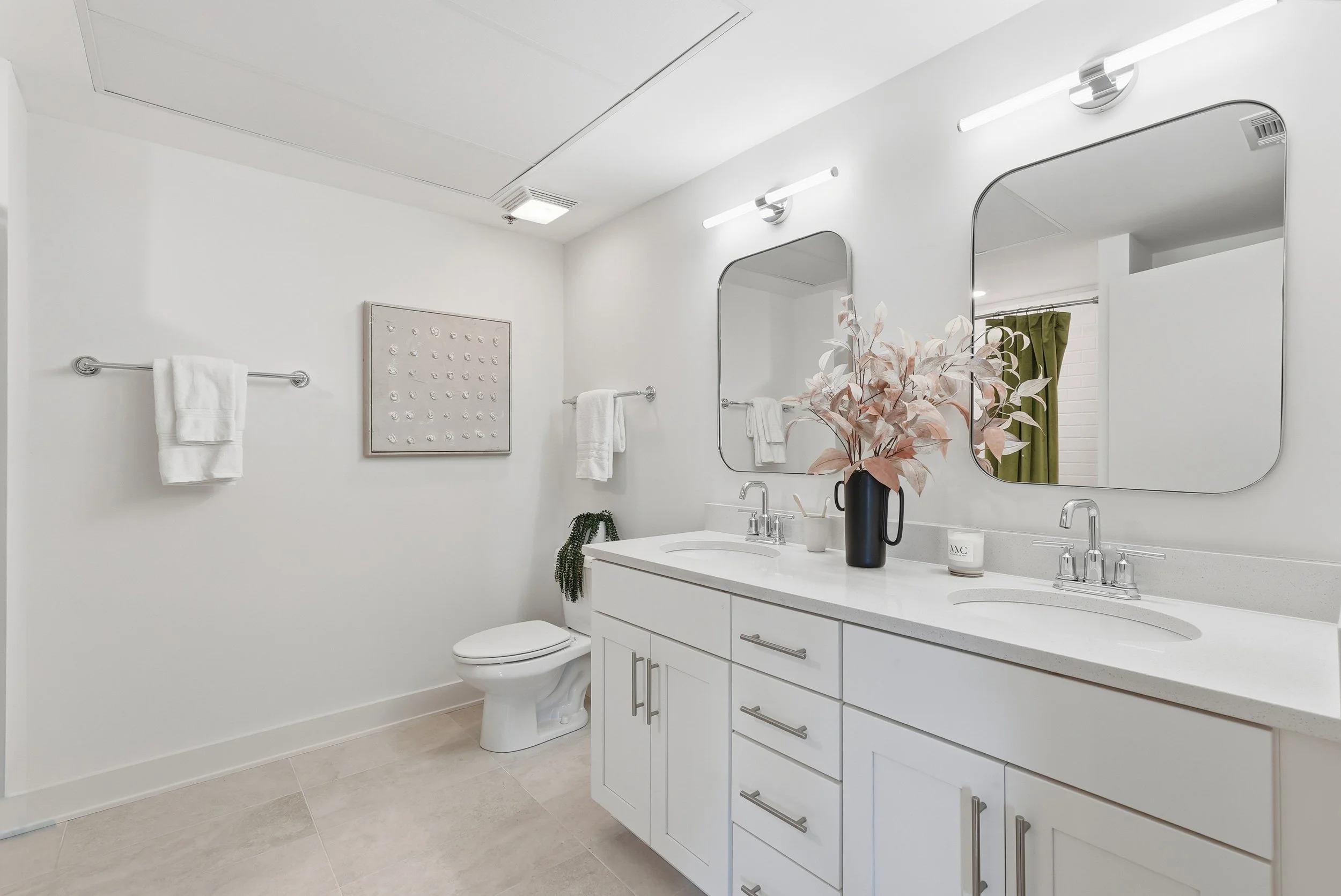 Modern bathroom with white vanity, two mirrors, and decorative vase with flowers.