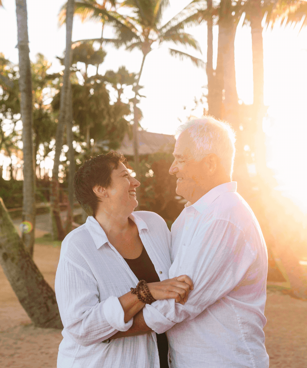 A happy older couple dancing outdoors at sunset, surrounded by palm trees.